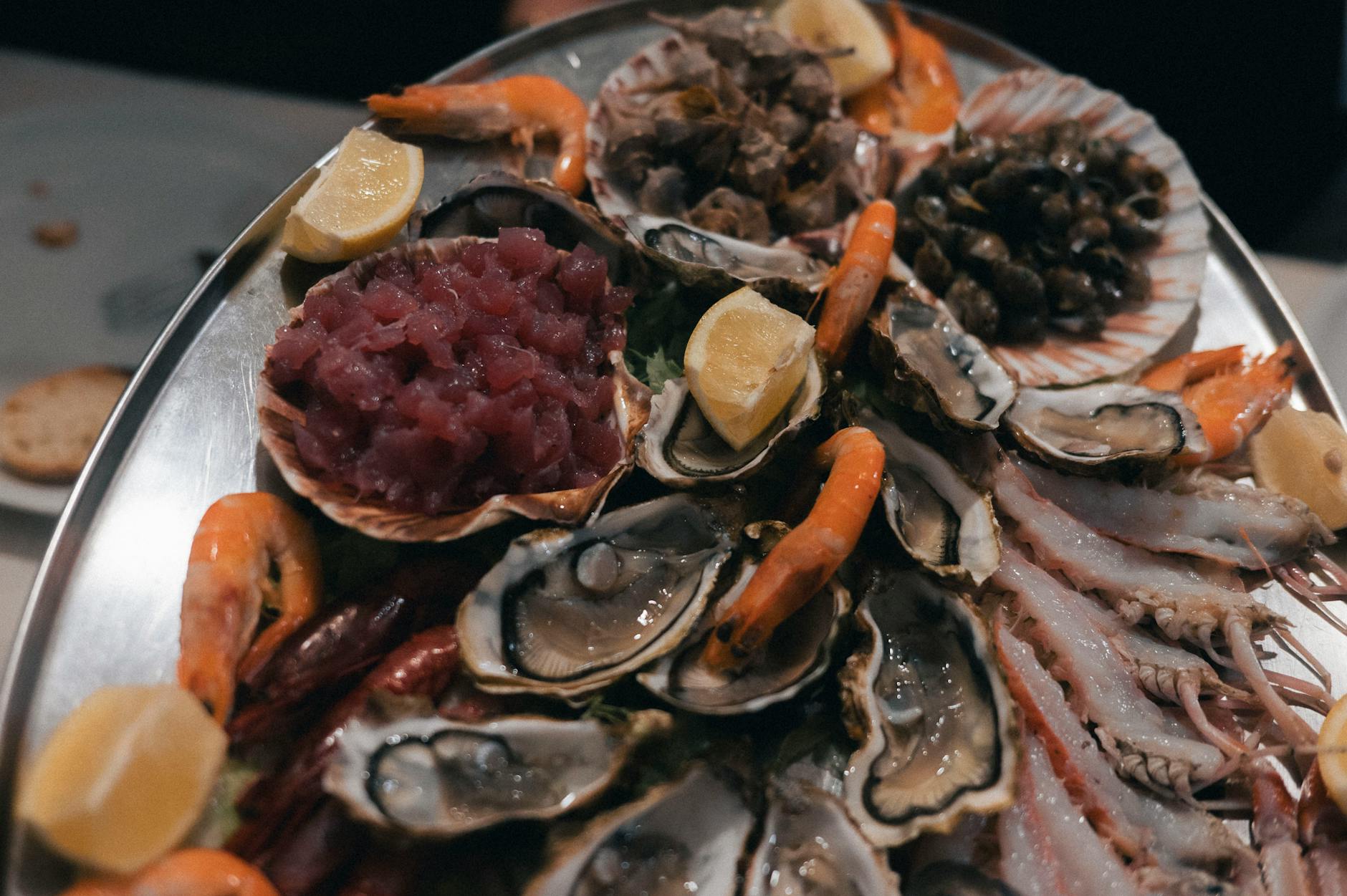 A beautifully arranged seafood platter featuring oysters, prawns, and tuna tartare with lemon garnish.