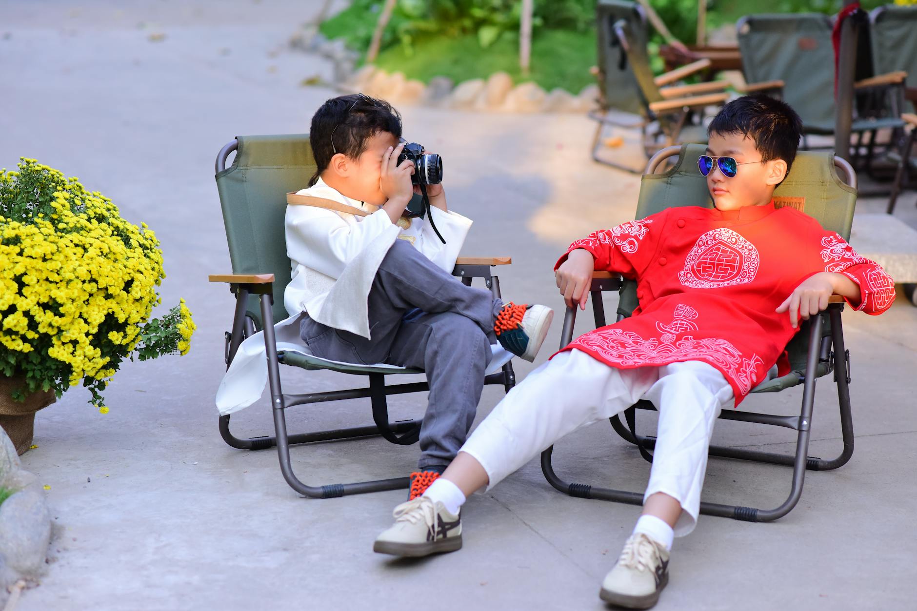 Two kids in traditional clothing enjoy leisure time outdoors, one taking photos.