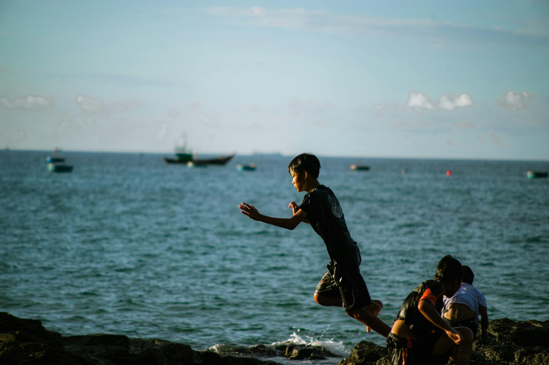 Children enjoy playful moments at the seaside, jumping and exploring on a sunny day.