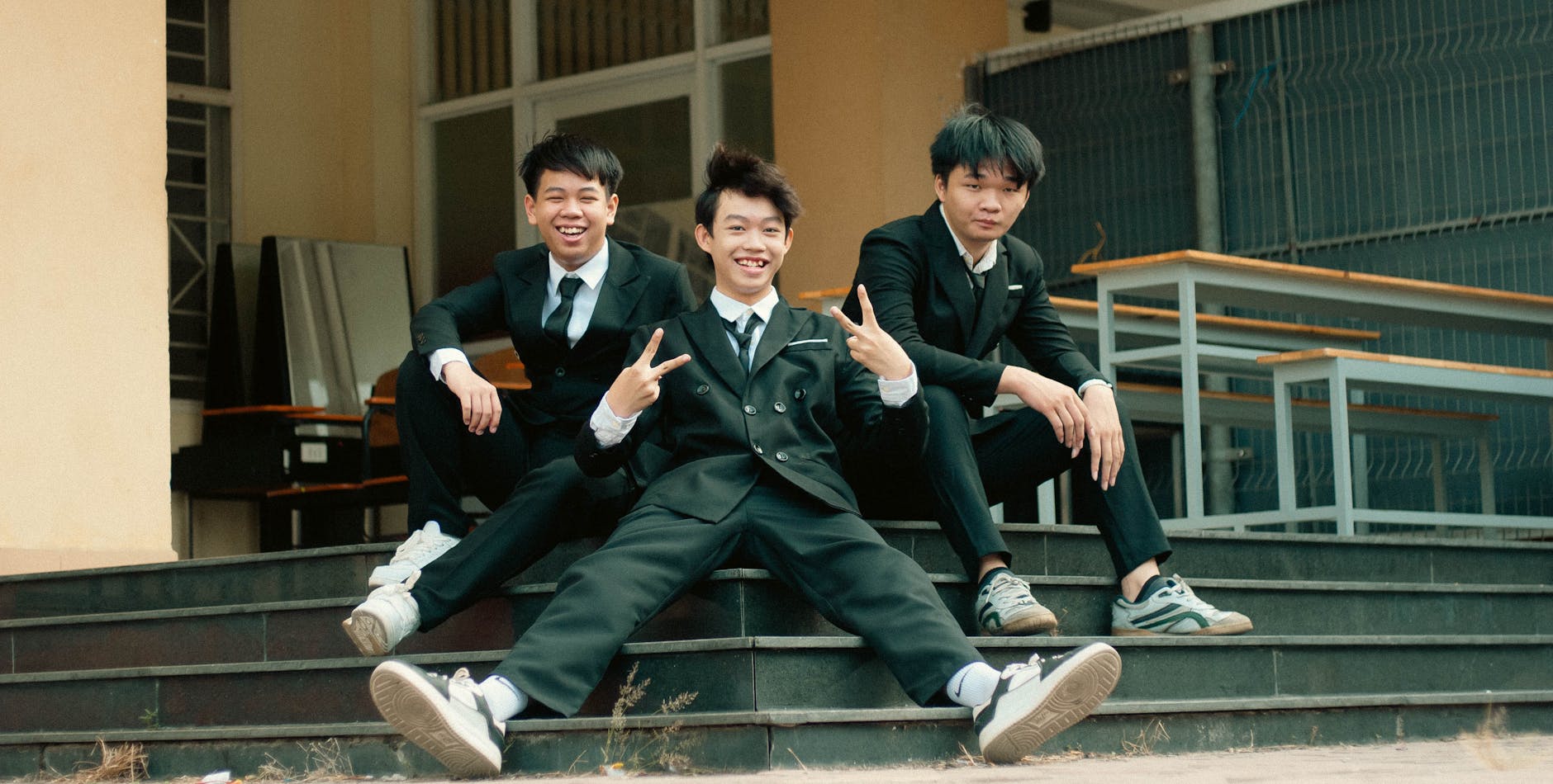Three young men in suits smiling and posing on outdoor steps.