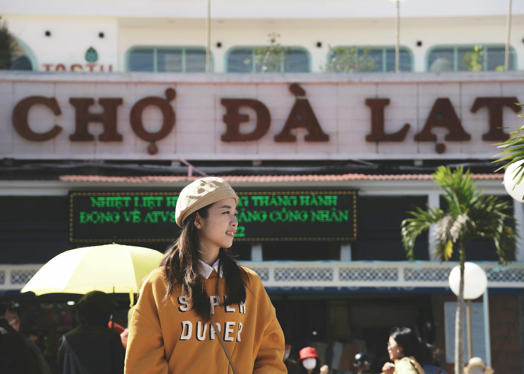 Asian woman enjoying a sunny day at Da Lat Market, smiling warmly.