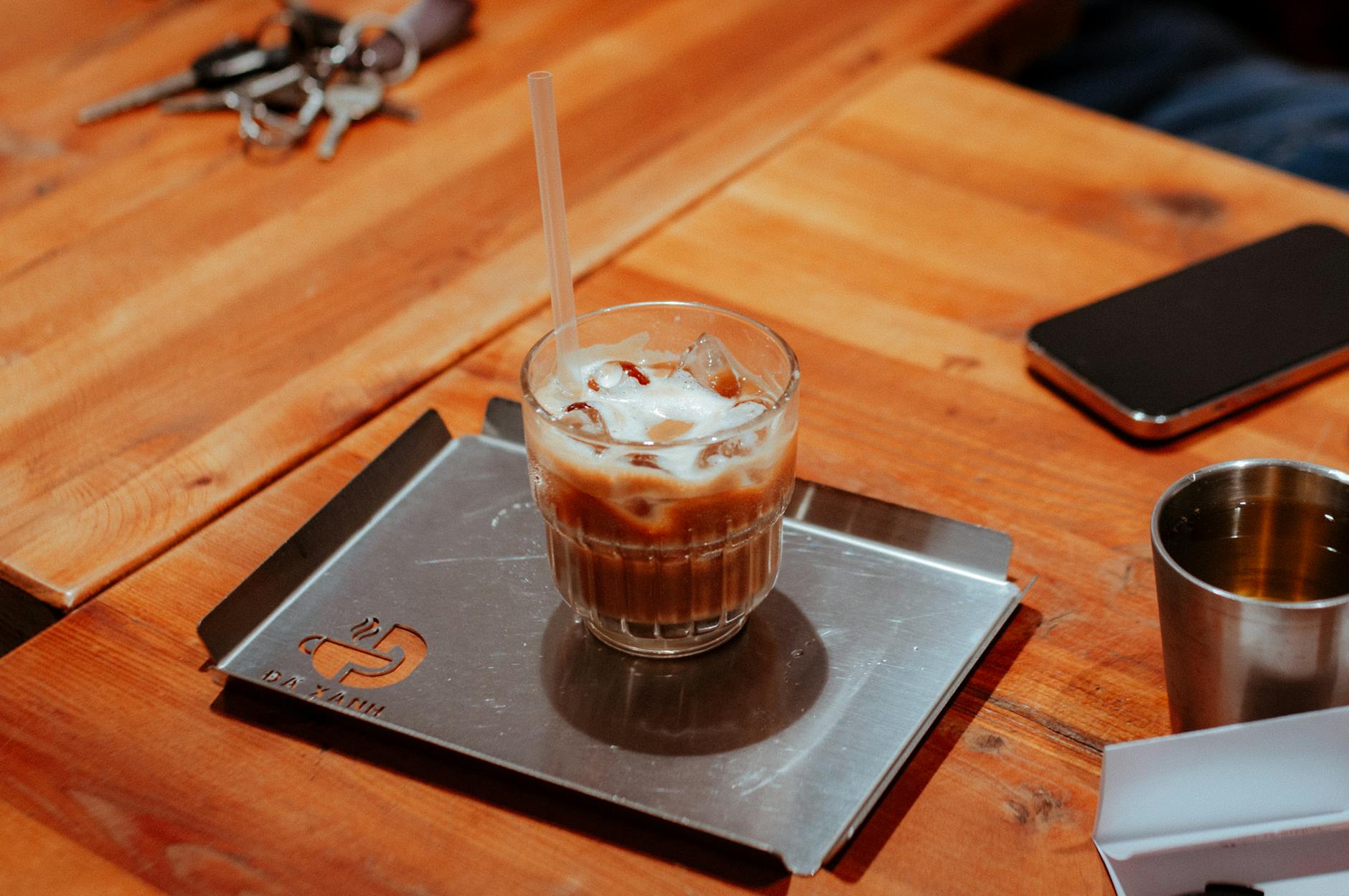 Refreshing iced coffee in a glass cup on a modern metal tray in a cozy café setting.