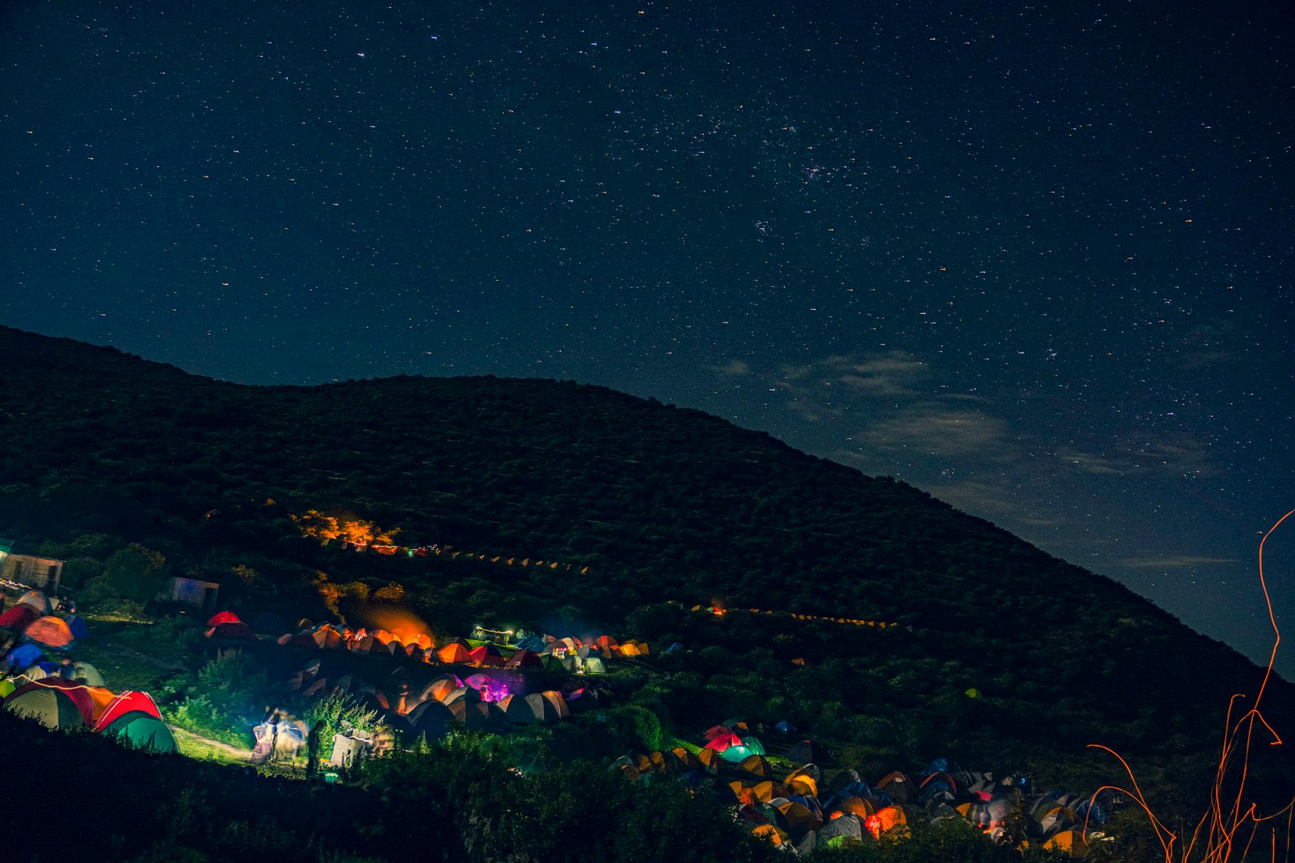 Tents illuminate the landscape under a vibrant starry sky, perfect for serene night camping adventures.