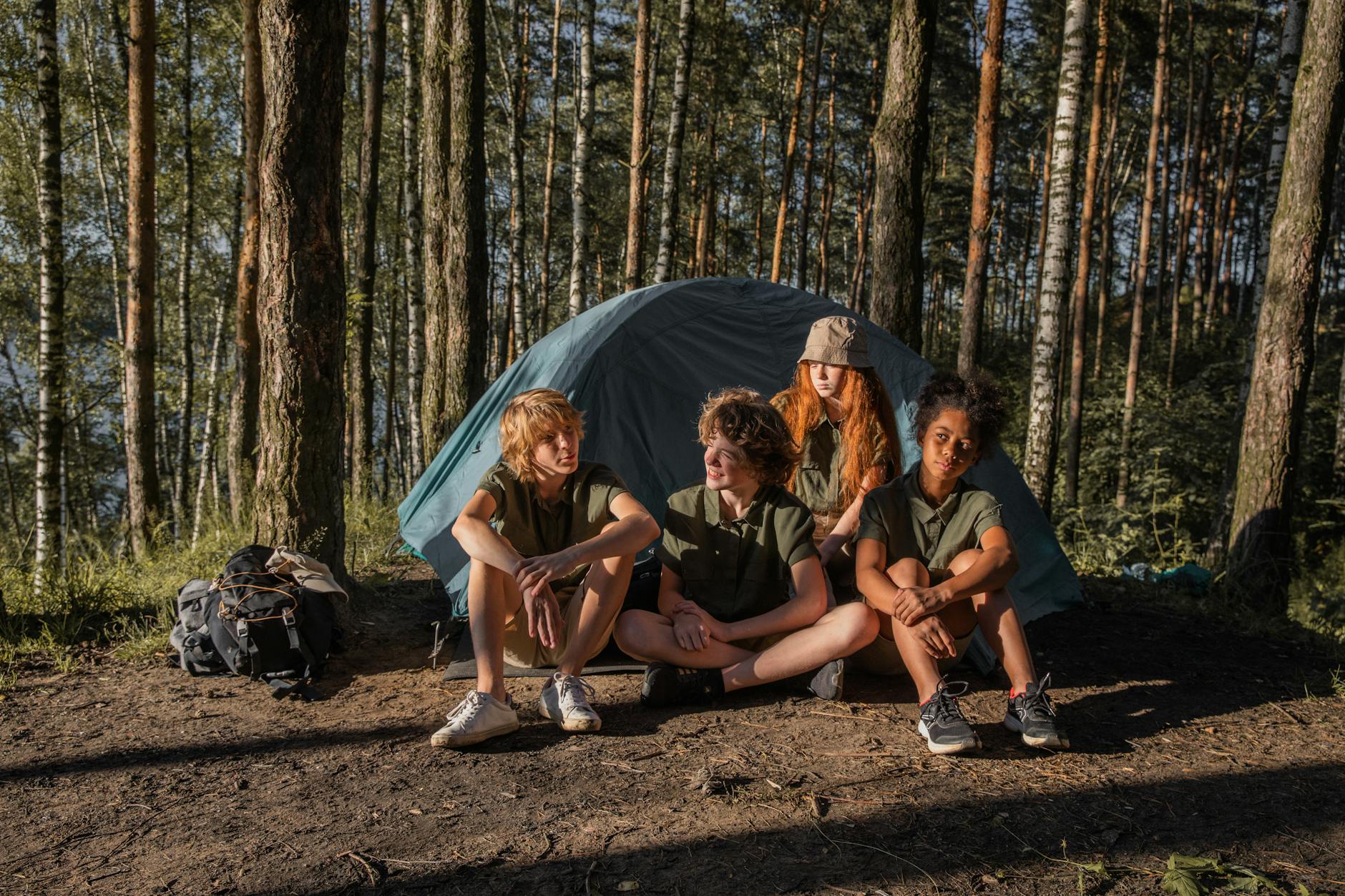 Four children sitting by a tent in the forest enjoy a camping adventure.