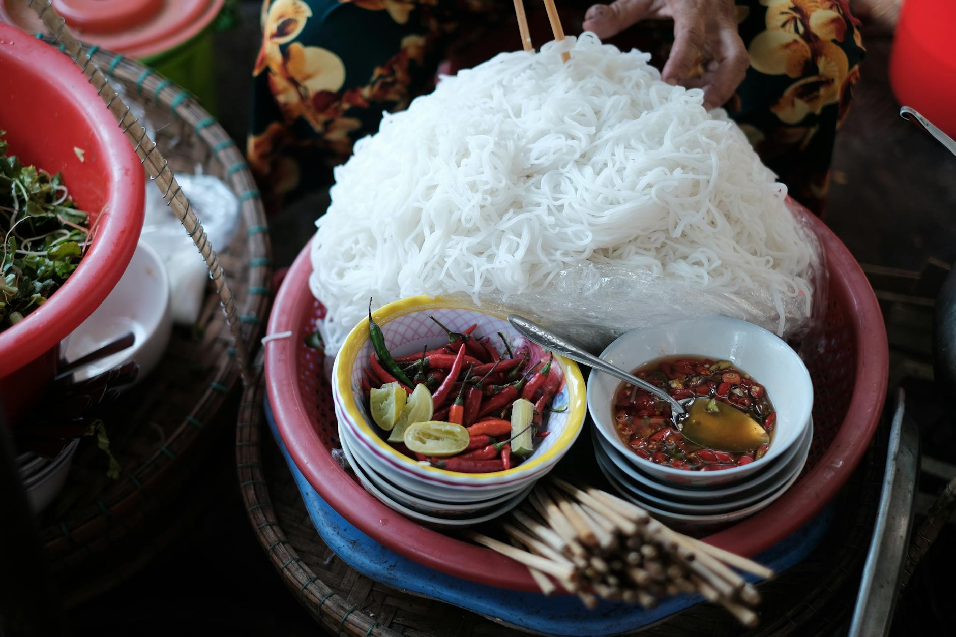 Vietnamese noodles with fresh herbs, chili peppers, and fish sauce captured in a market setting in Hue, Vietnam.