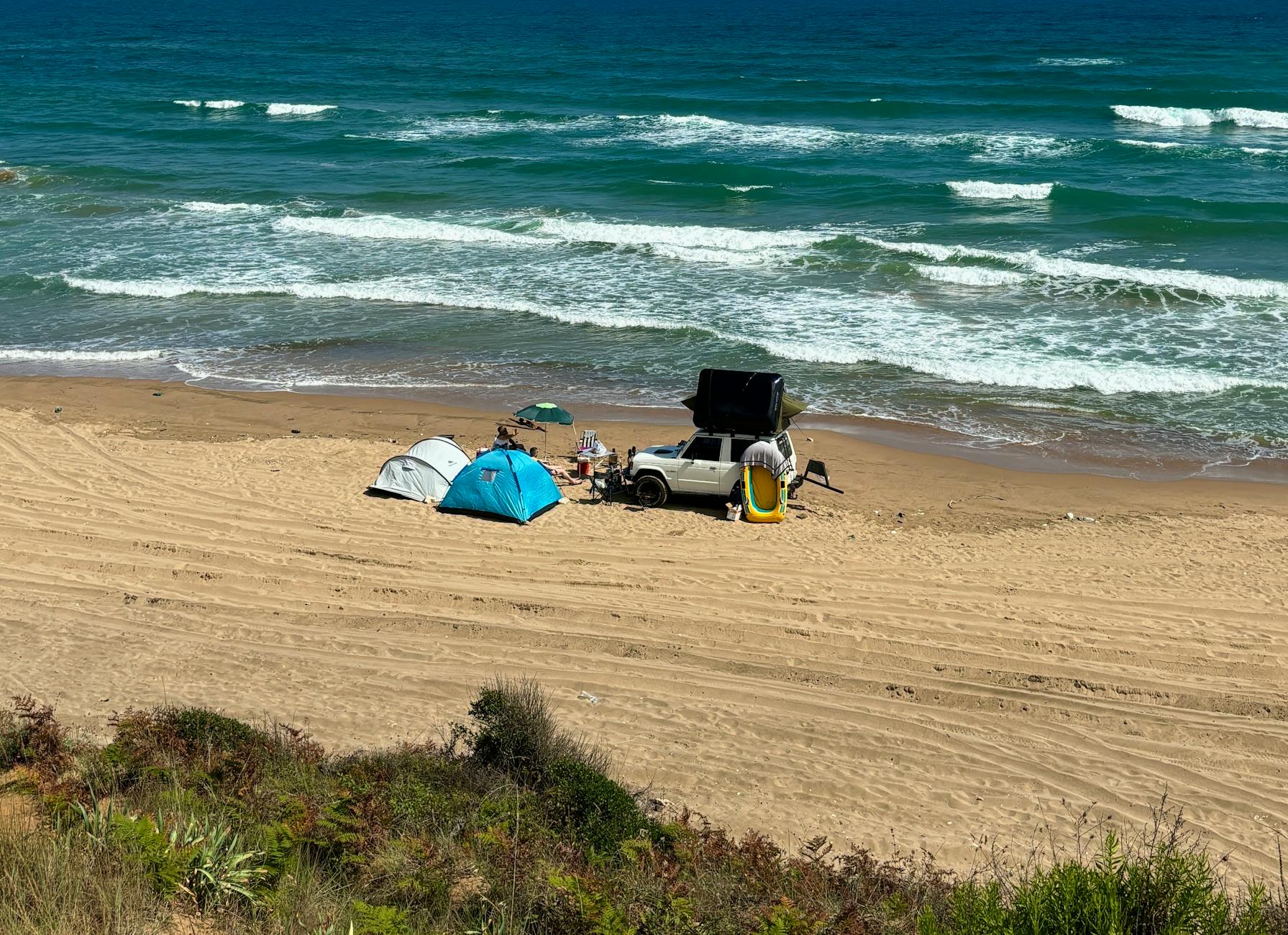 Tents and SUV on a scenic sandy beach with ocean waves, perfect for a beach camping adventure.