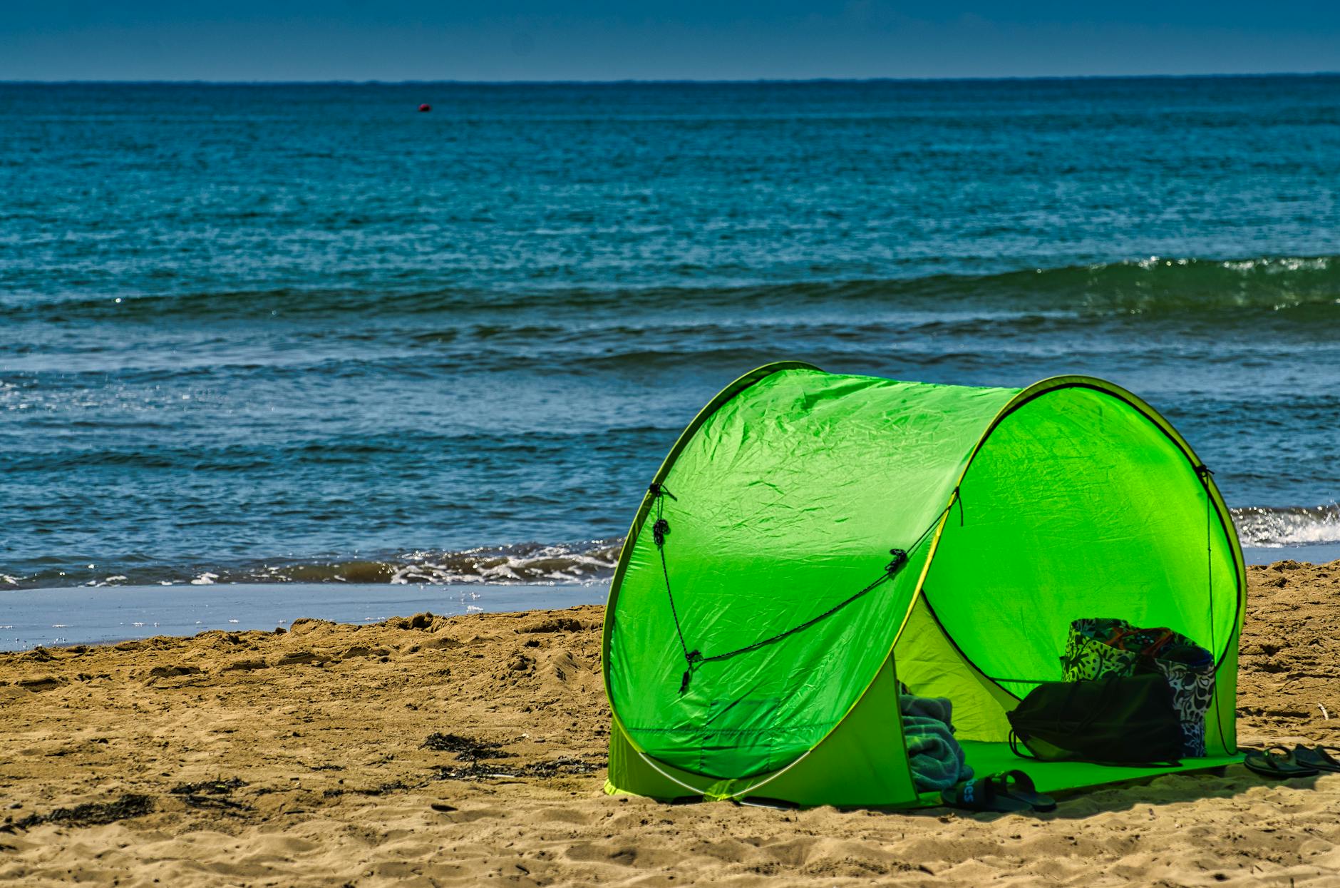 A vibrant green tent on a golden sandy beach by the blue ocean. Perfect for seaside leisure.