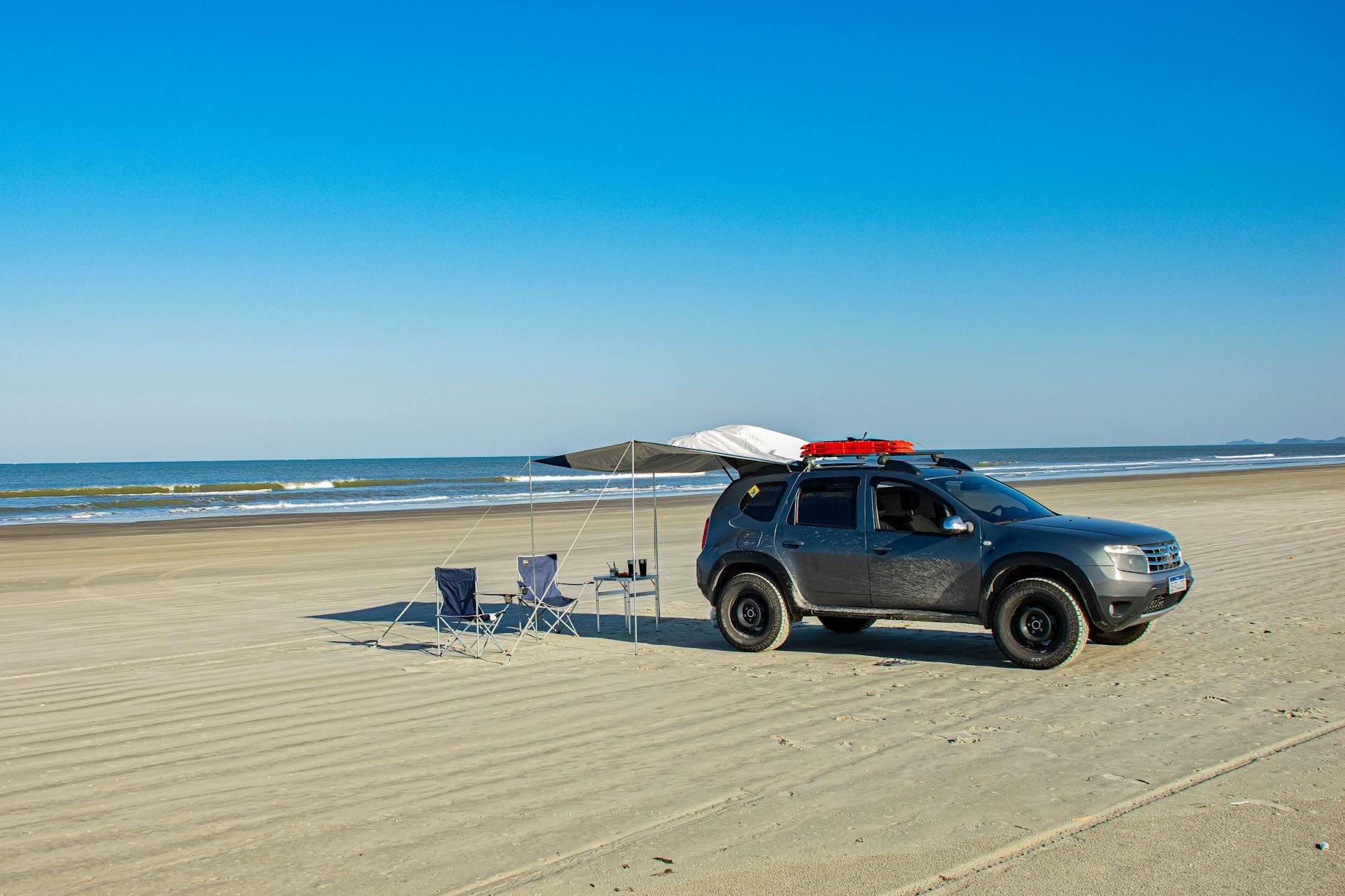 A car parked on Ilha Comprida beach with camping gear under a clear blue sky.