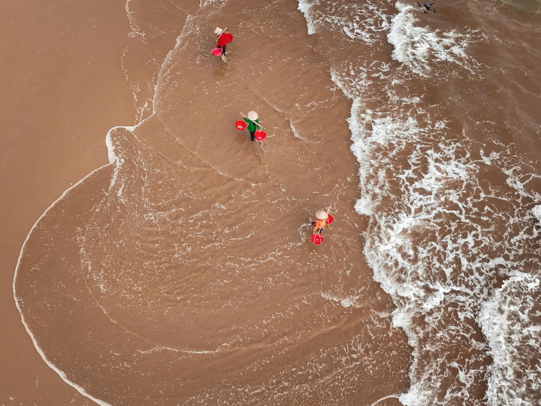 Fishermen with traditional hats working on the beach in Hội An, Vietnam, from an aerial perspective.