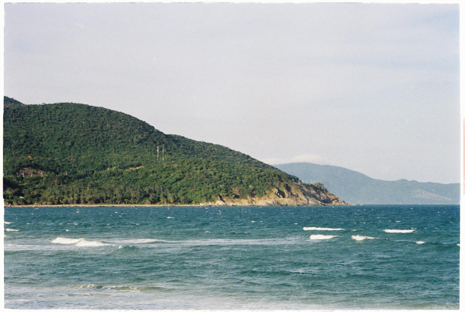 A serene coastal landscape featuring lush green hills and blue sea at Cam Ranh, Vietnam.