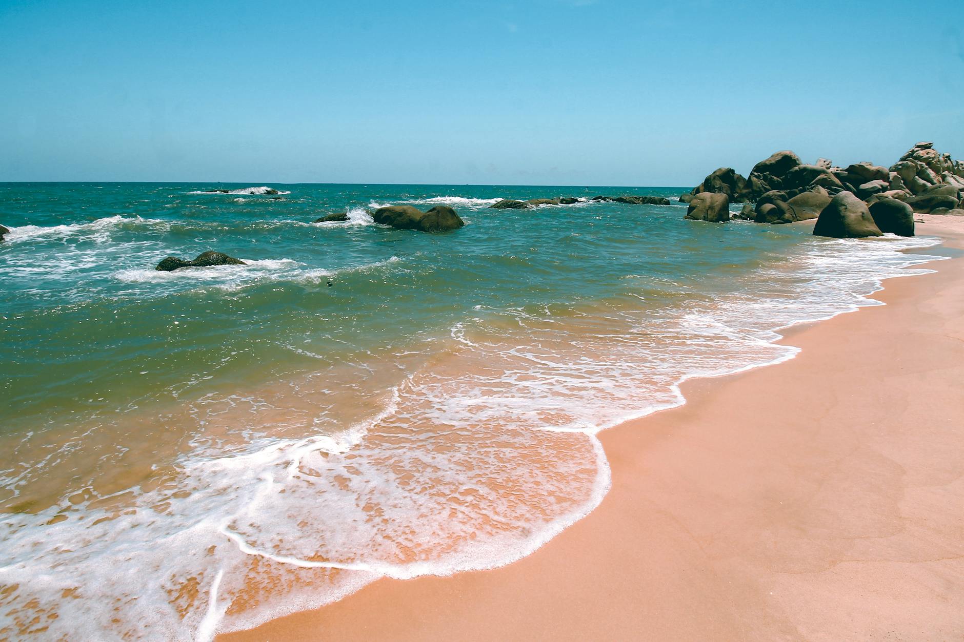 Serene beach view in Nha Trang, Vietnam with gentle waves lapping the sandy shore and rocky formations.