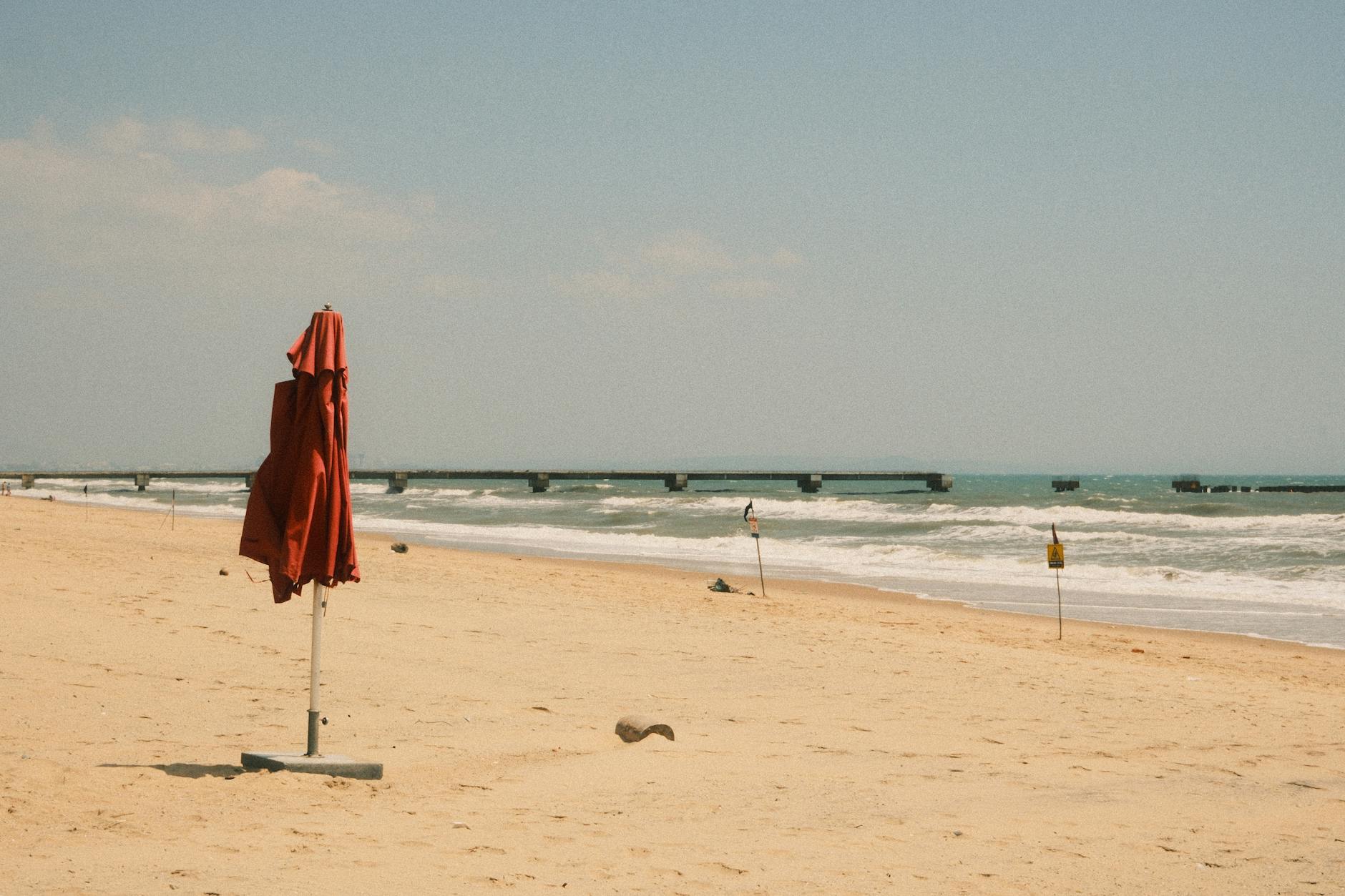 Peaceful view of Phan Thiet beach, Vietnam with a red umbrella and waves gently lapping the shore.
