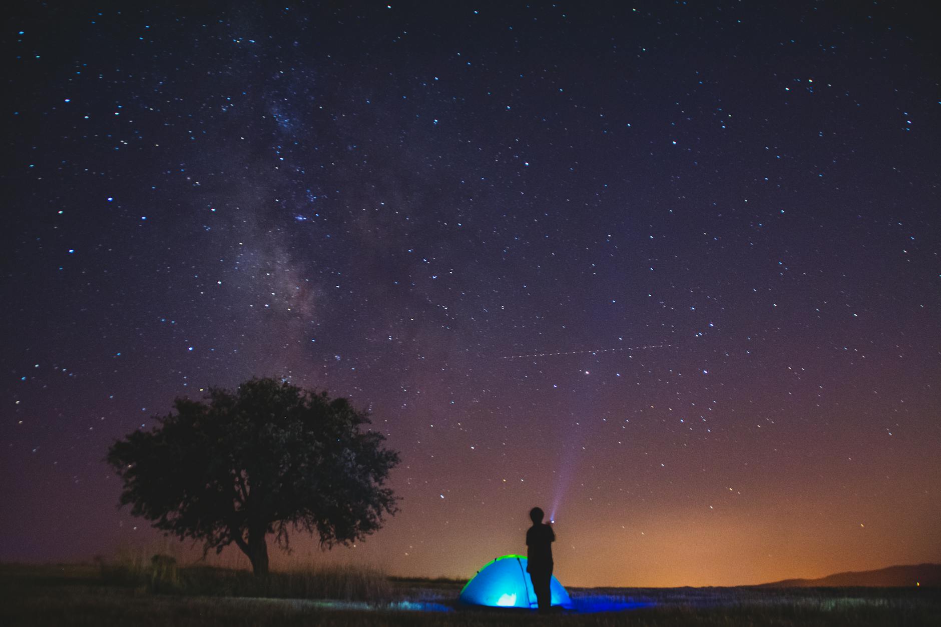A person camping under a starry sky with the Milky Way visible.