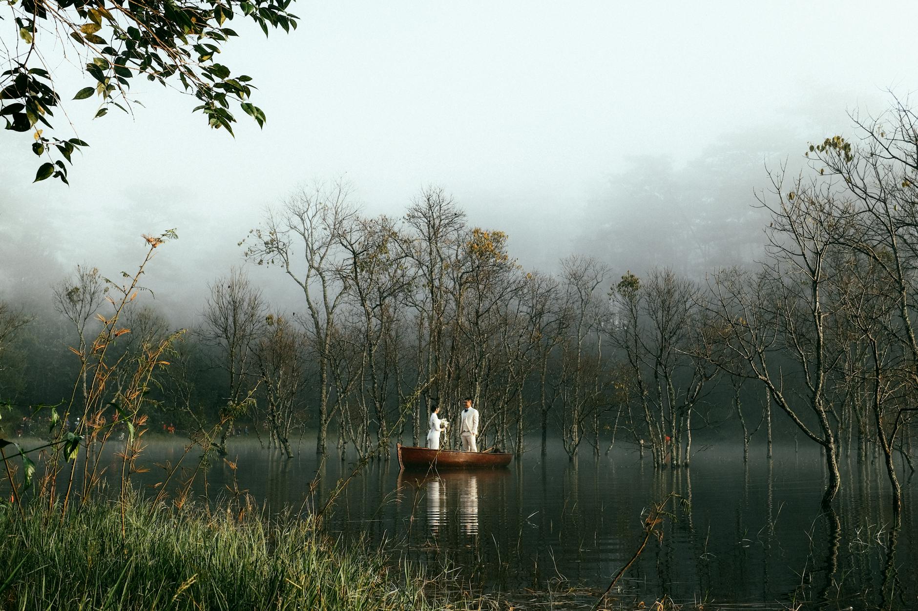 A calm morning scene of a couple in a boat on a misty lake in Dalat, Vietnam.