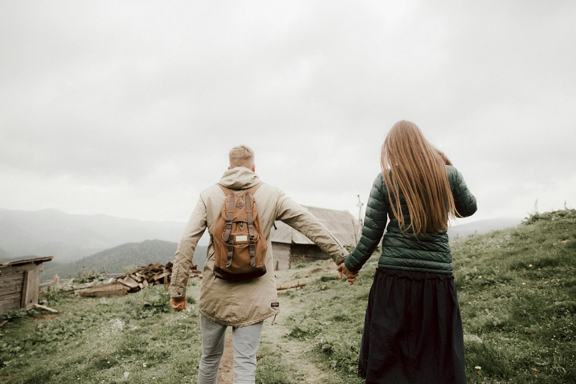 A couple walking hand in hand on a scenic foggy mountain path, surrounded by nature.