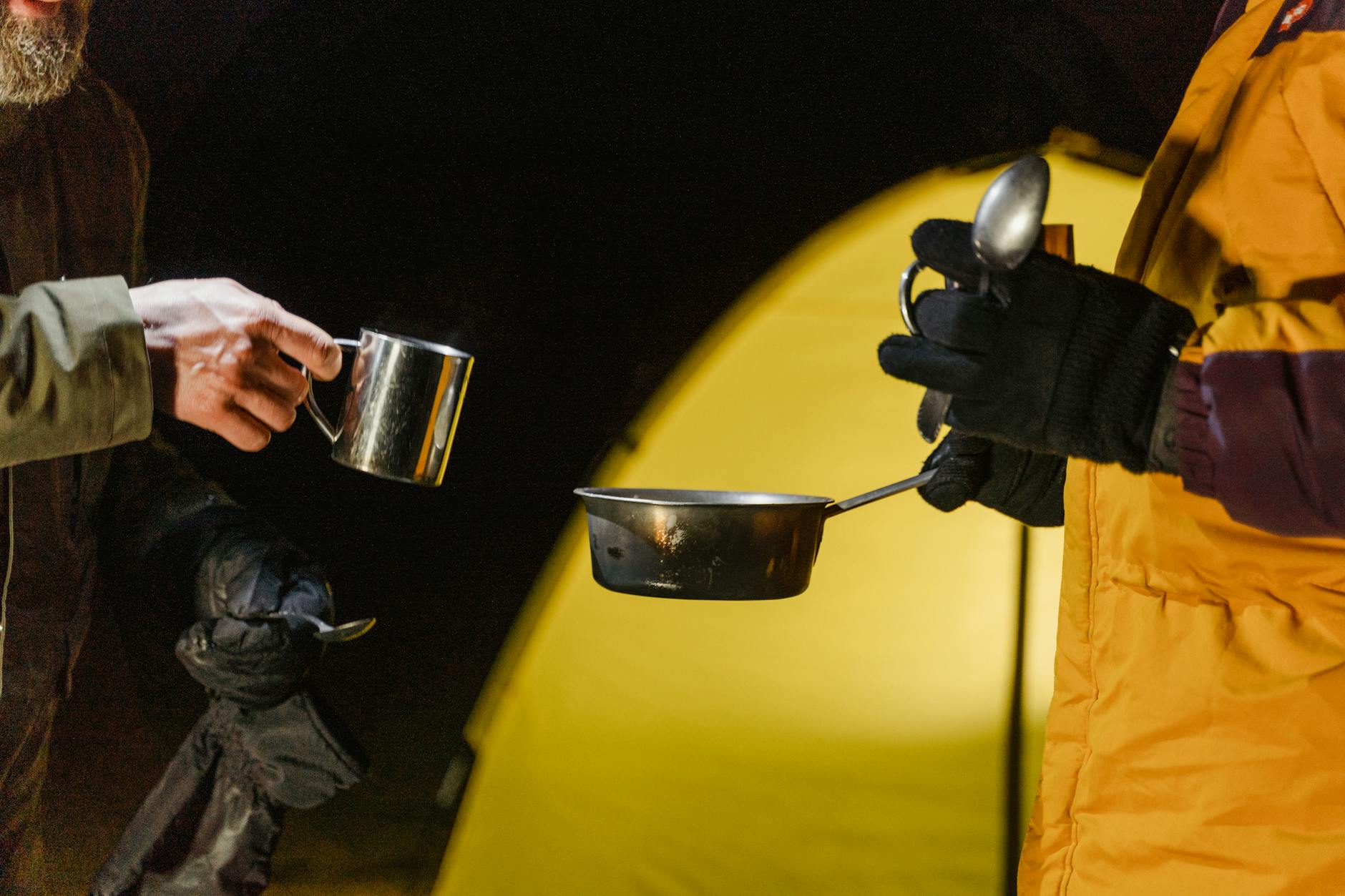 Two campers preparing a warm meal outdoors in winter, with a cozy tent backdrop.