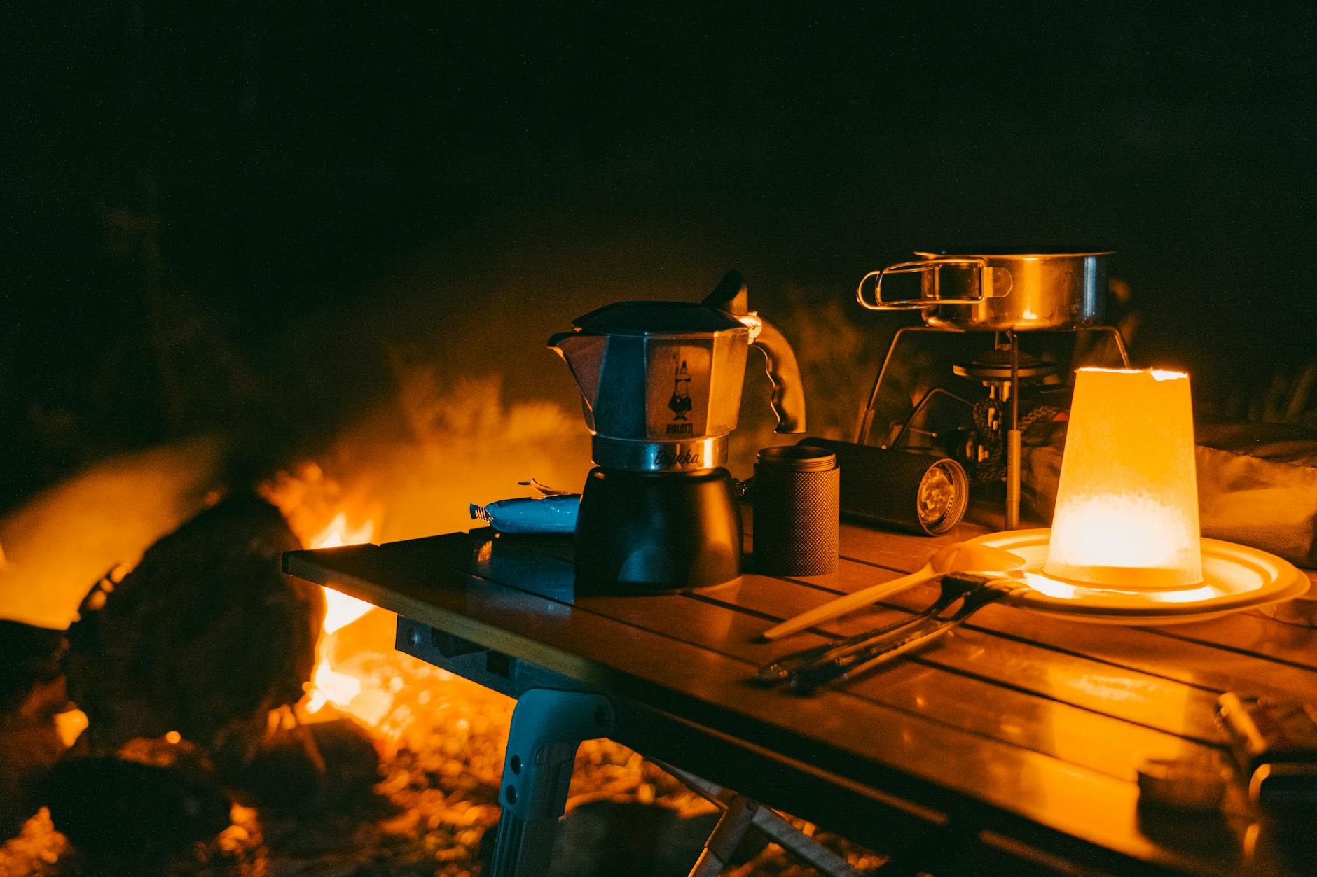 A warm and intimate campfire setting with a coffee maker and cooking gear, perfect for outdoor adventures.