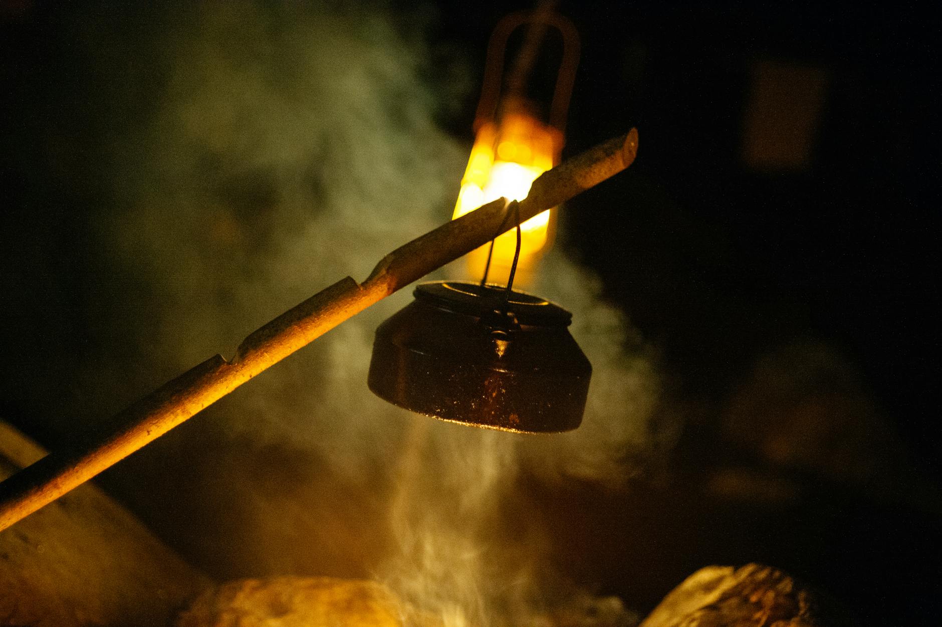 Rustic night scene of a kettle hung over a campfire, creating warm ambiance.
