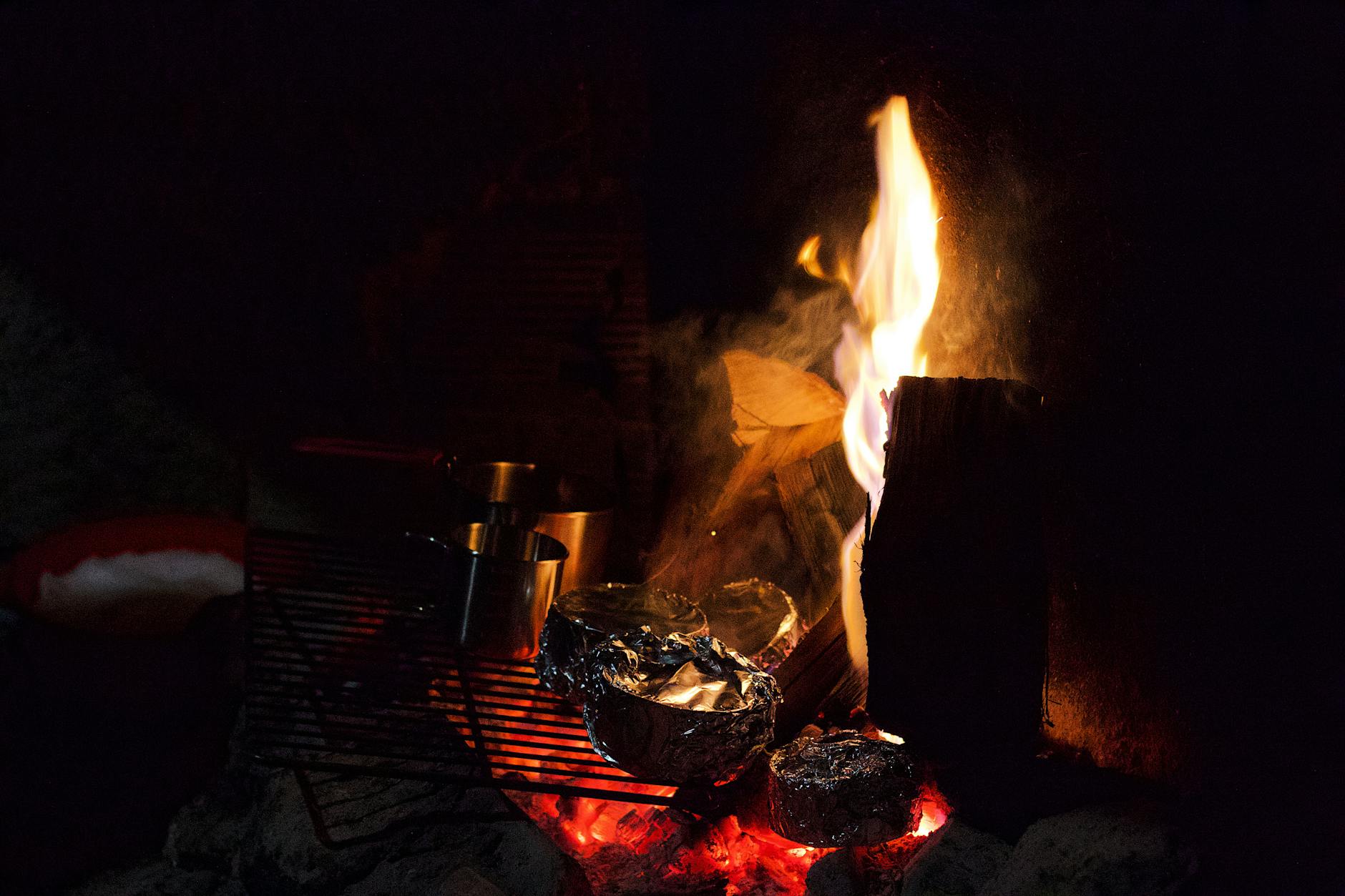 A warm bonfire with flames and foil-wrapped food on a grill. Perfect for camping and outdoor cooking visuals.