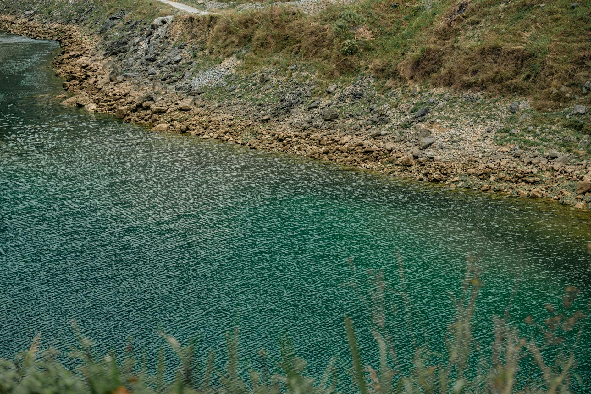 Calm shoreline scene featuring clear turquoise waters and rocky terrain.