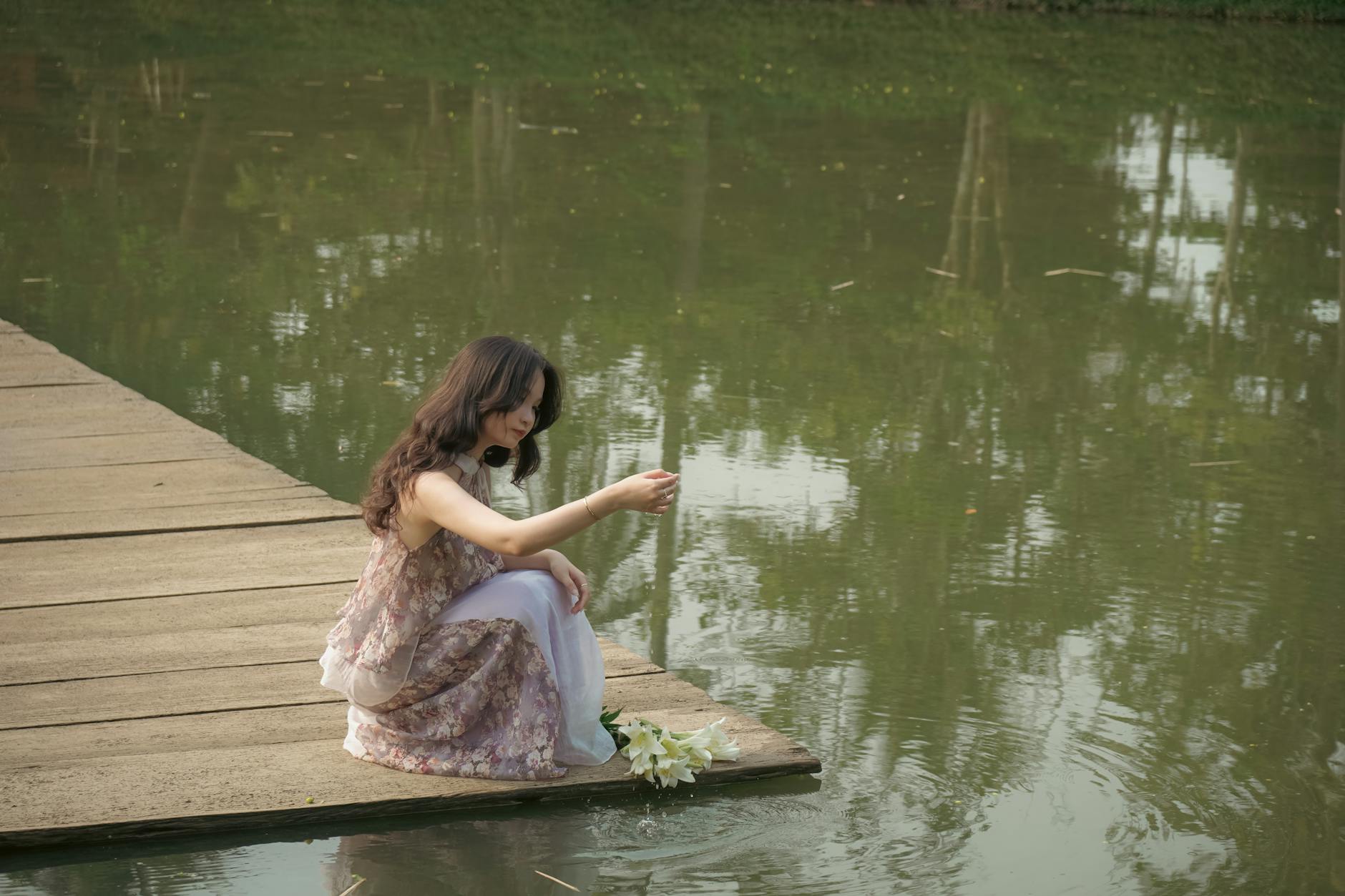 Asian woman sitting on a pier with white lilies, reflecting serenity in a Ho Chi Minh City park.
