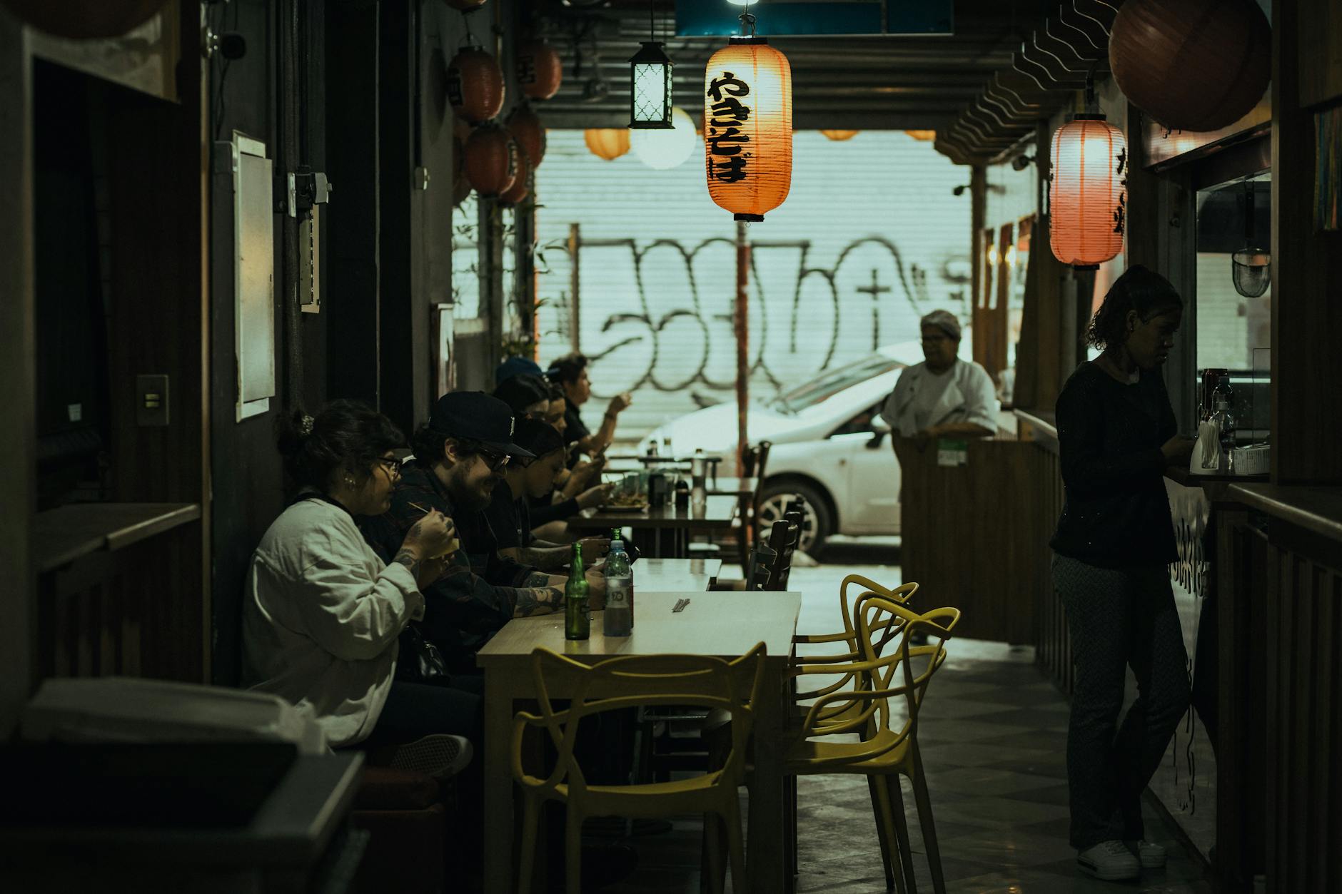 Dimly lit Asian restaurant interior with patrons enjoying dining under hanging lanterns.