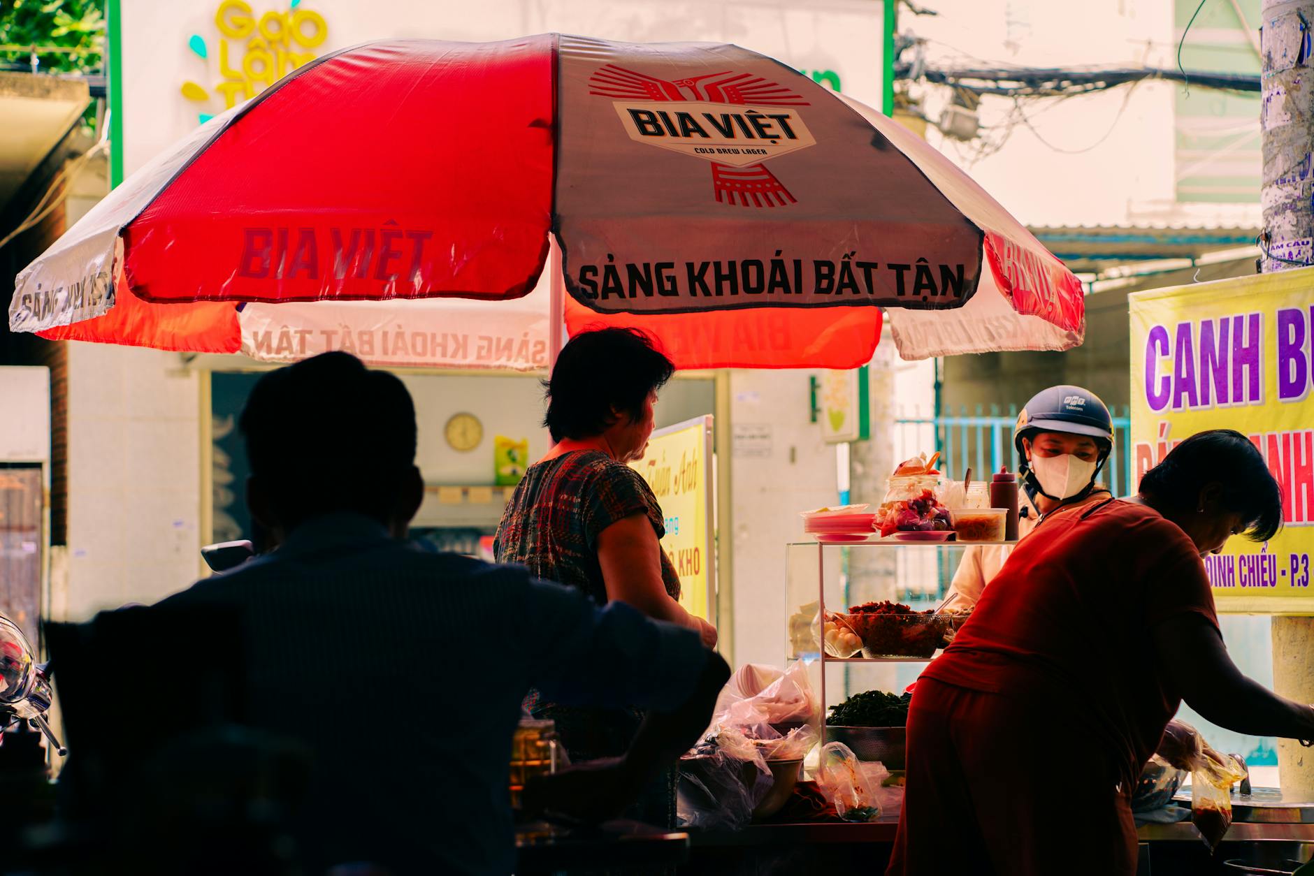 Street food vendors under red umbrella in vibrant Ho Chi Minh City, Vietnam's bustling market scene.