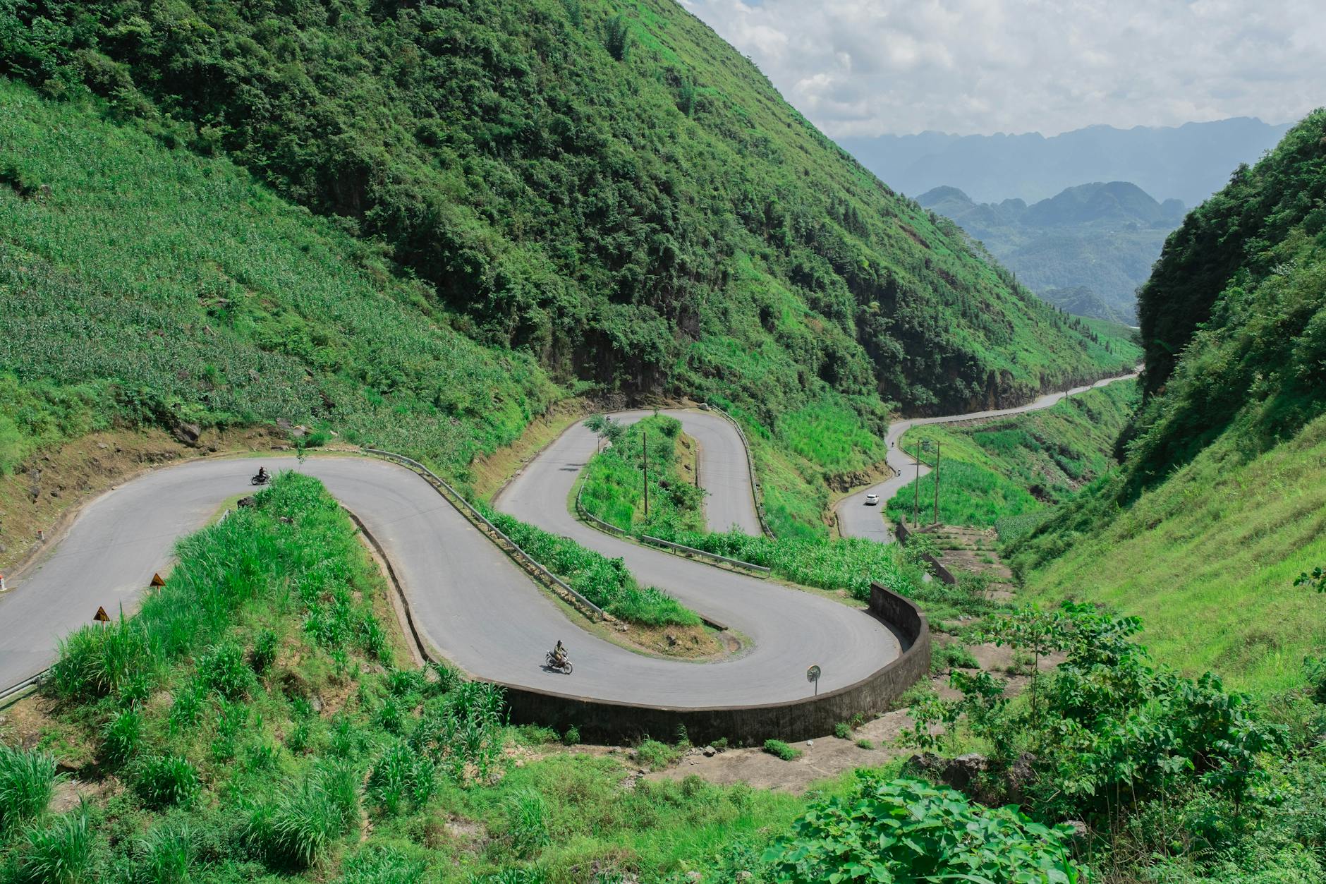 Aerial view of a winding road cutting through lush green mountains in Hà Giang, Vietnam.