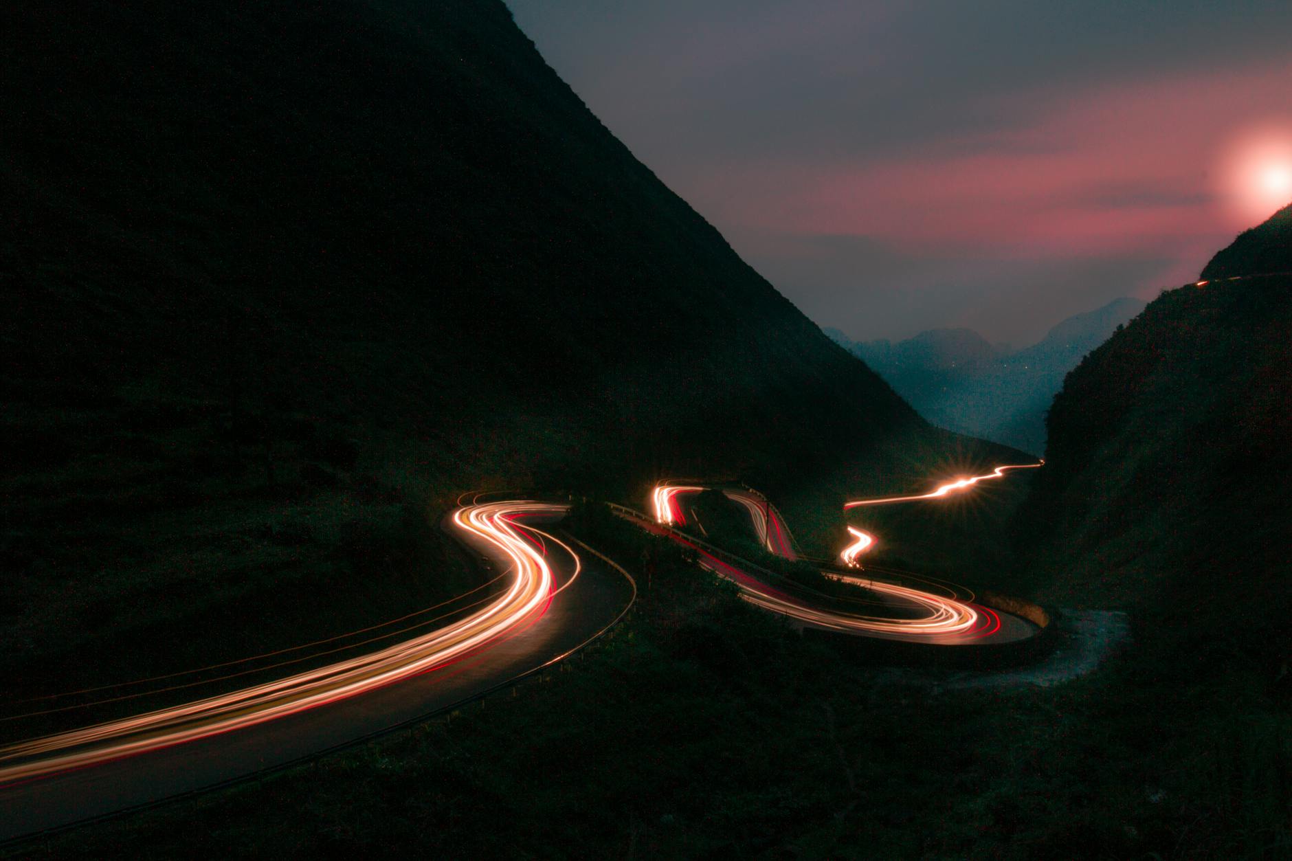 Long exposure of car light trails winding through Ha Giang mountain pass at dusk, Vietnam.