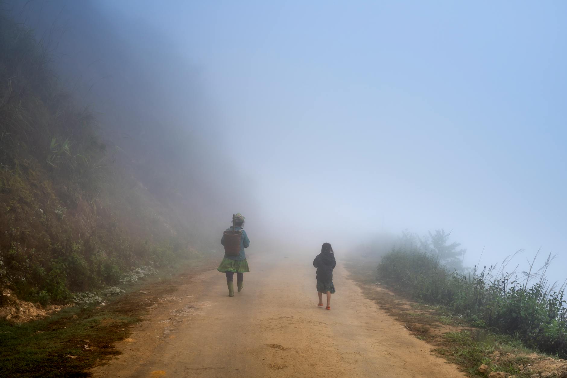 Distant anonymous little local children strolling on rural roadway near grassy mountain in gloomy weather in suburb area of countryside