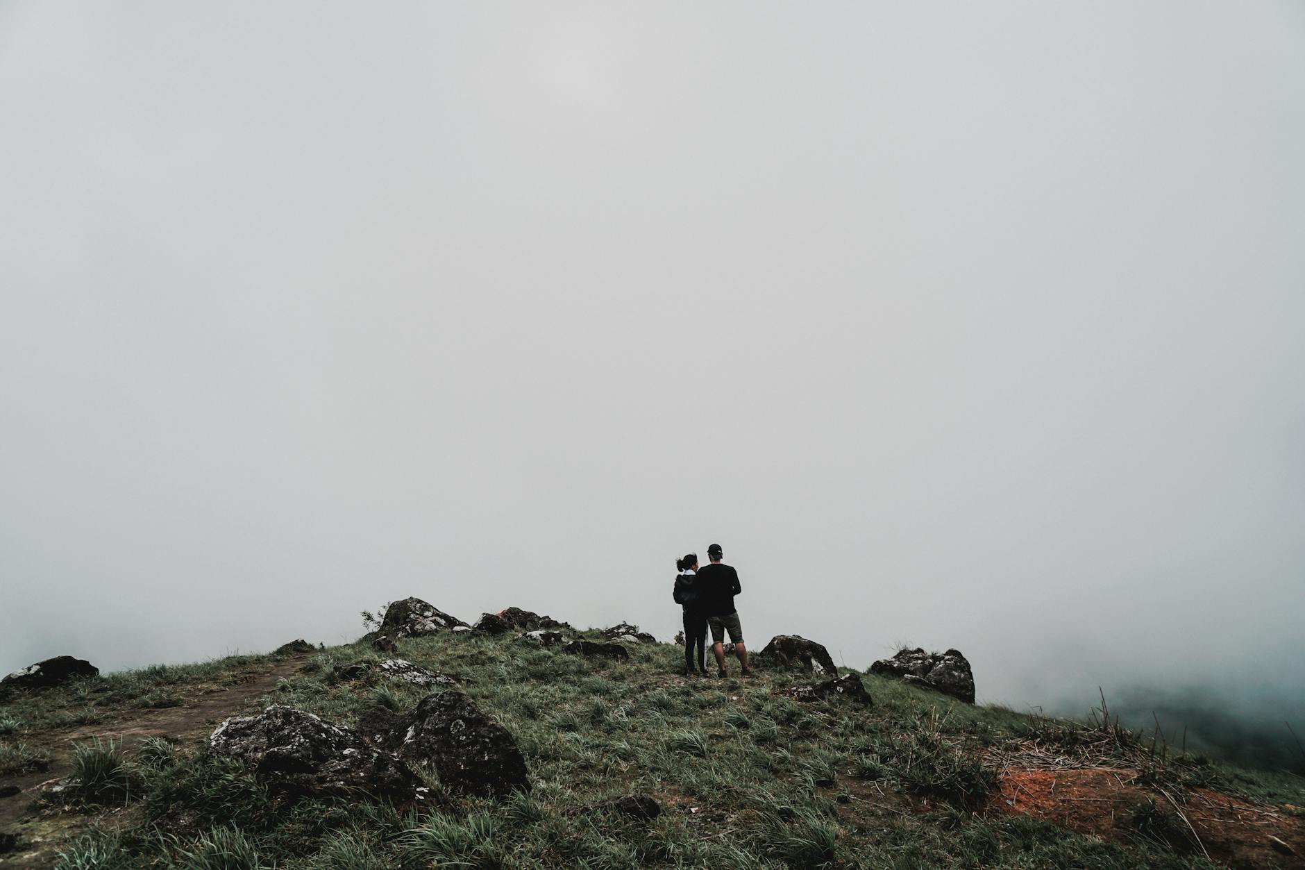 A couple standing on a foggy hilltop, surrounded by mist and rocks.