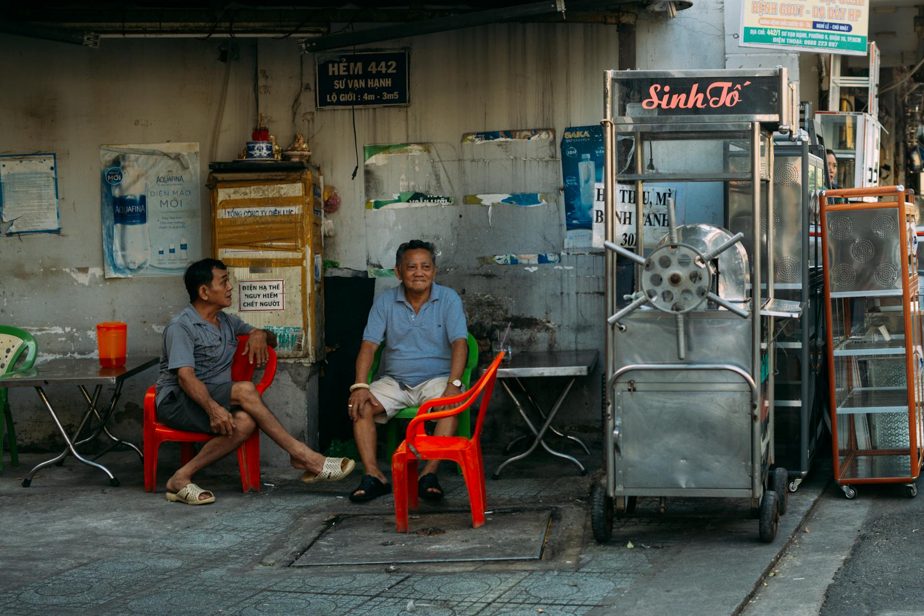 Two men sit by a street vendor stall, enjoying a day outdoors.