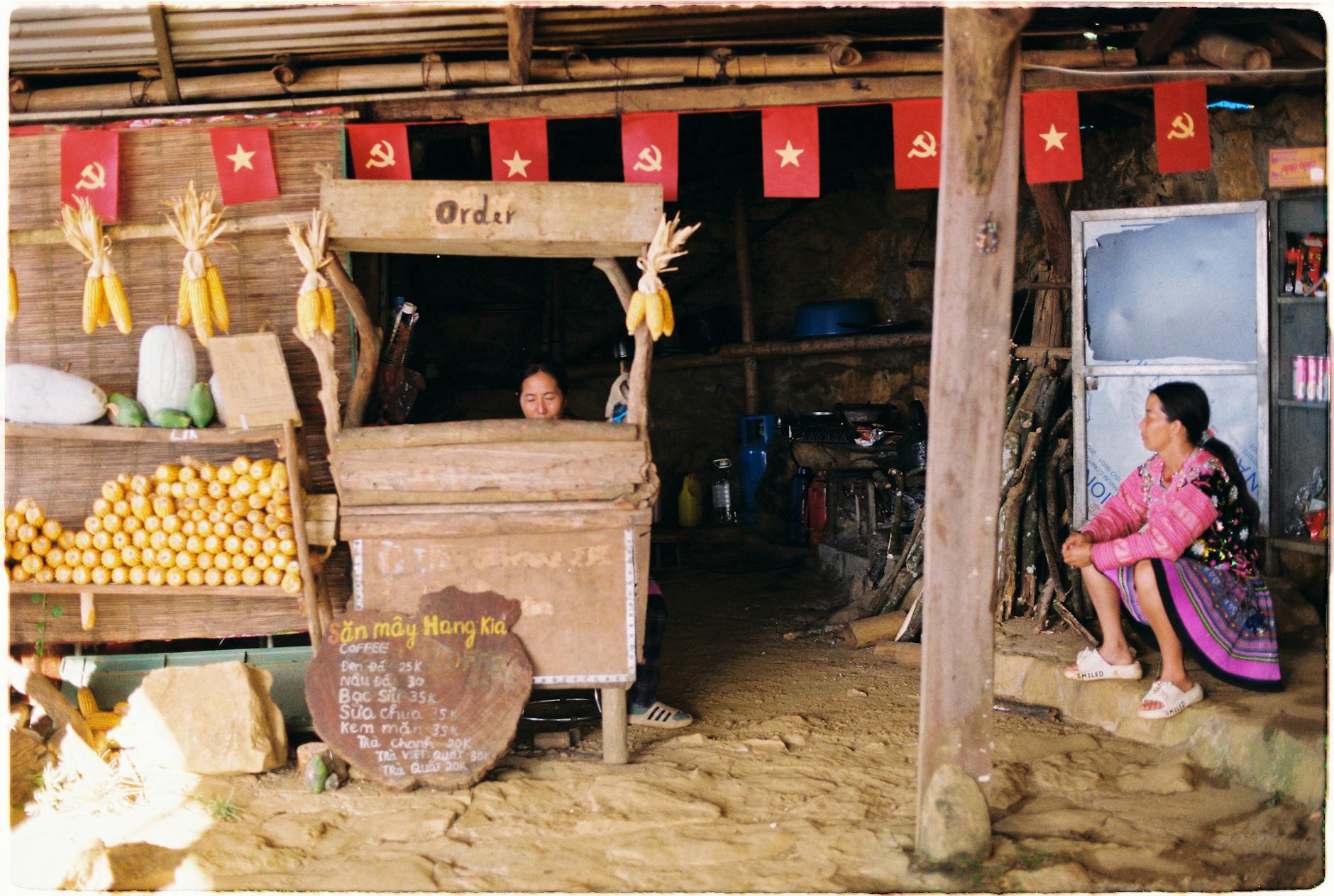 A rustic market stall displays local produce with two women present, evoking cultural heritage.