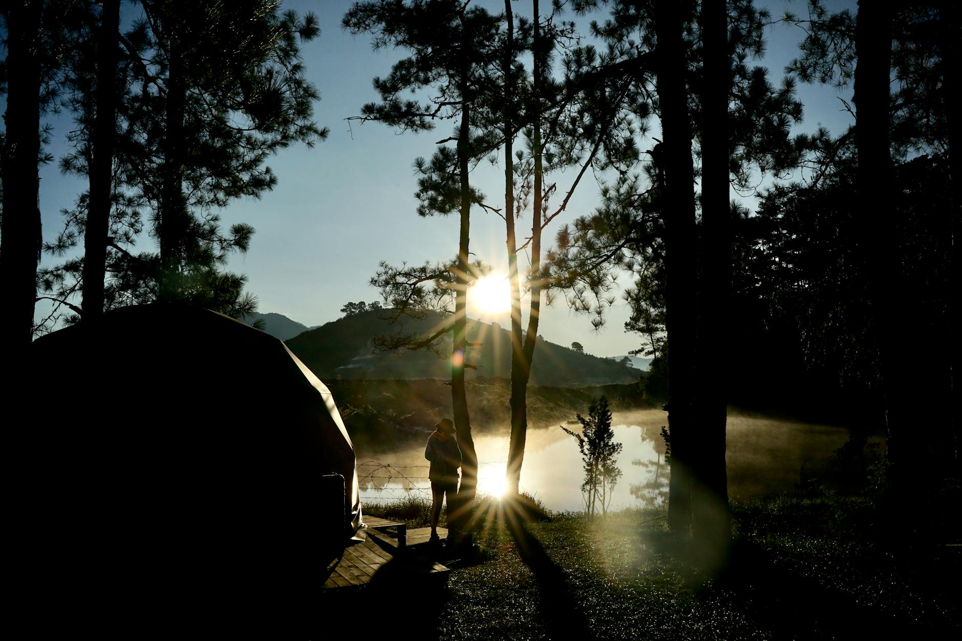 Experience the tranquility of sunrise reflections over a misty lake surrounded by trees in Dalat, Vietnam.
