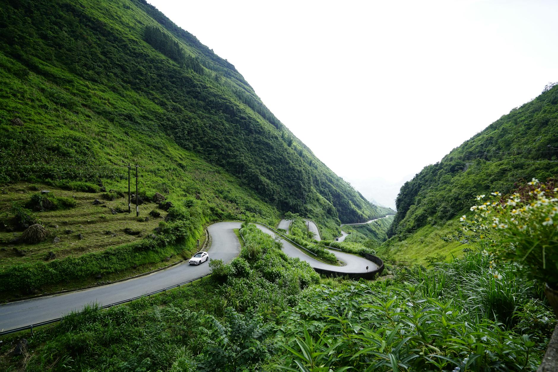 A winding road meanders through a lush green valley surrounded by mountains.