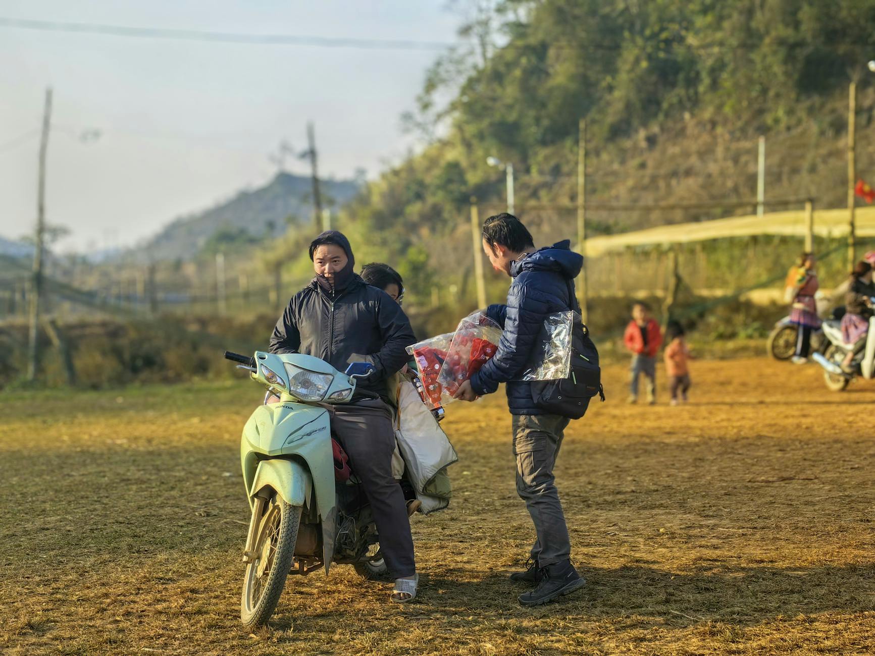 Locals interacting on a motorbike in a Vietnamese village setting.