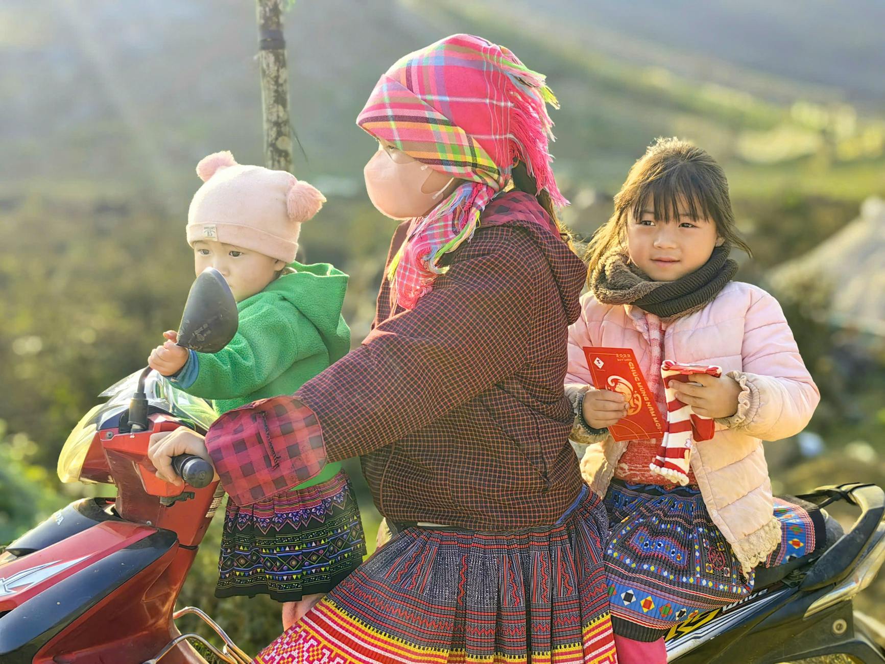 Young Vietnamese children riding a motorbike in Moc Chau, dressed in traditional clothing.