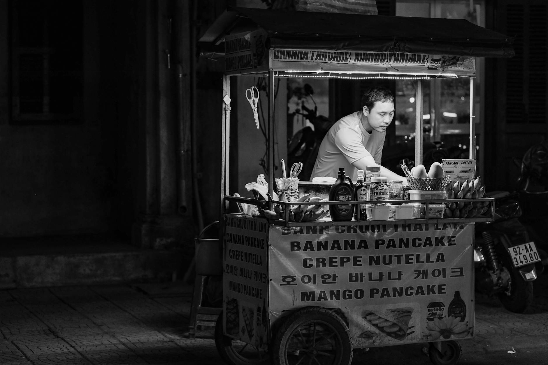 Black and white photo of a street vendor preparing pancakes in Hội An, Vietnam at night.