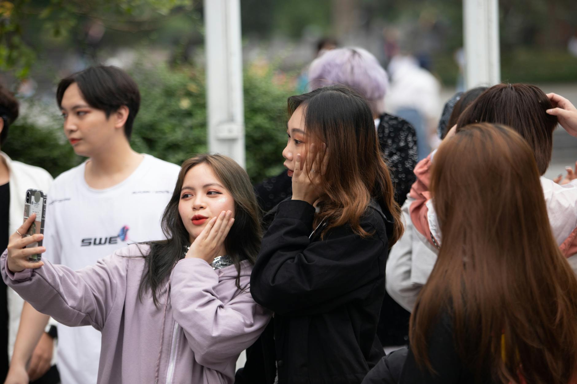 Group of young adults taking a selfie outdoors, capturing a fun and casual moment.
