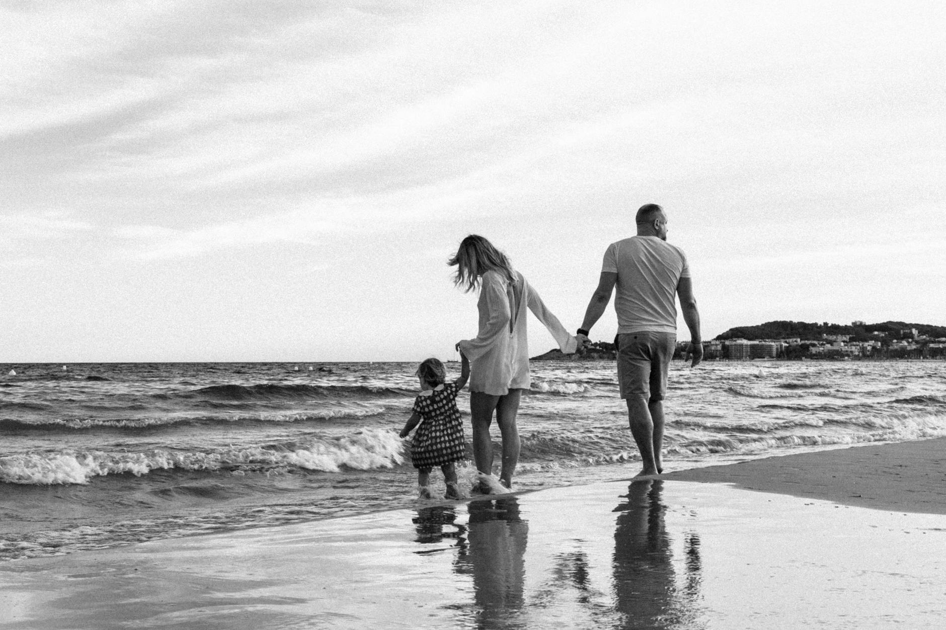 A family enjoys a peaceful walk along the beach with gentle waves.