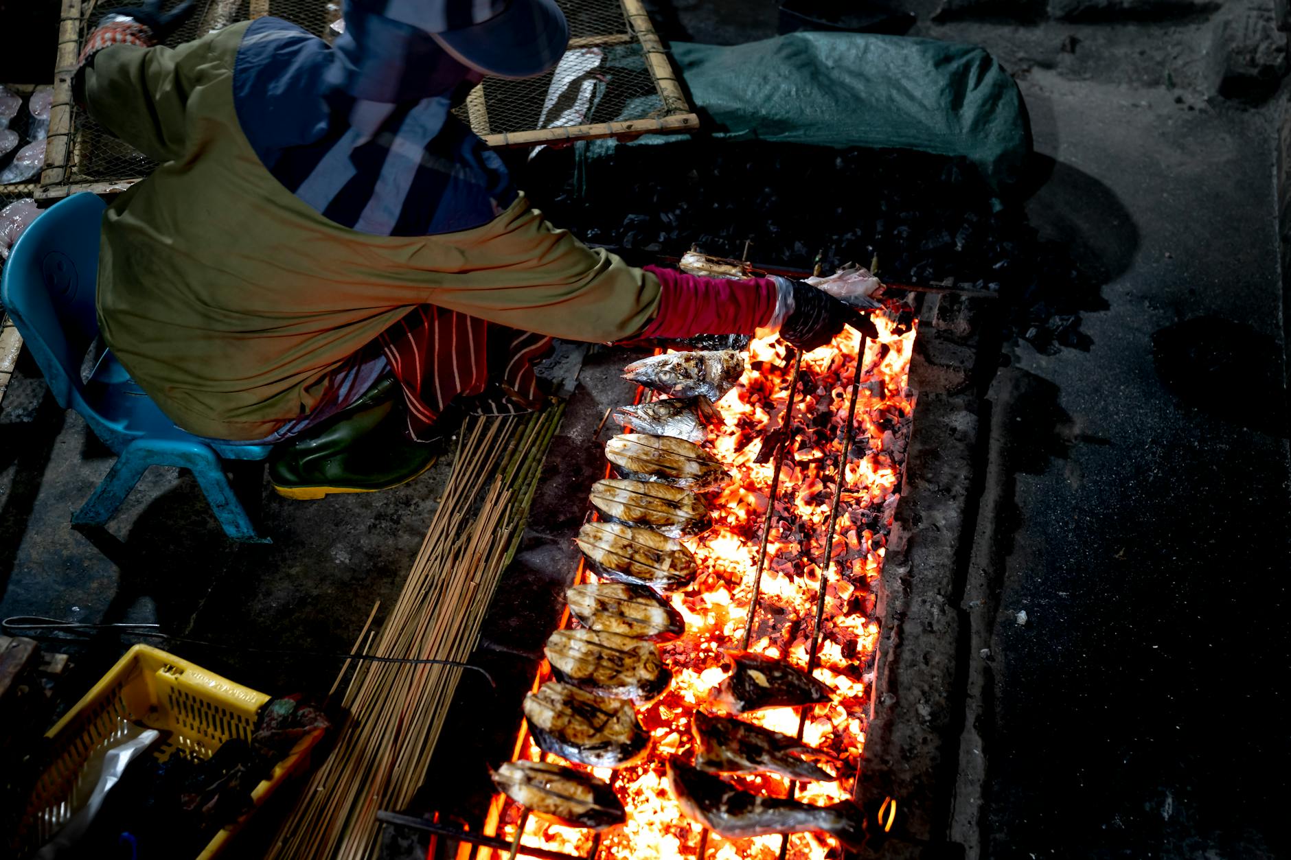 A street vendor grills fresh fish on a charcoal fire, capturing traditional cuisine's essence.