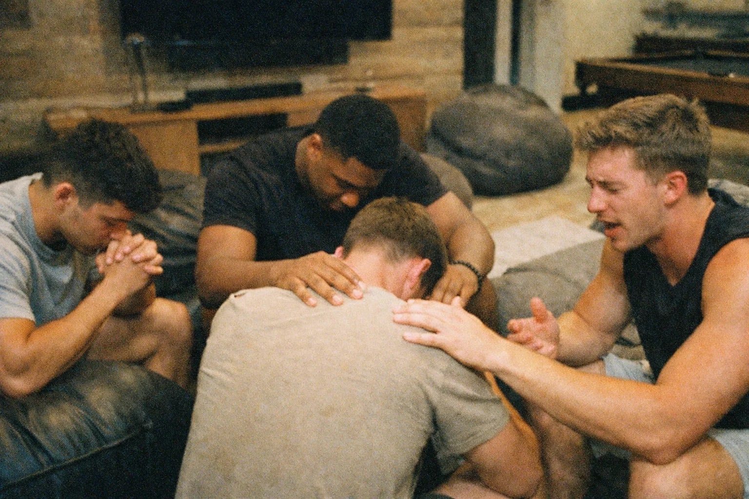 Four men in a prayer circle at The Den