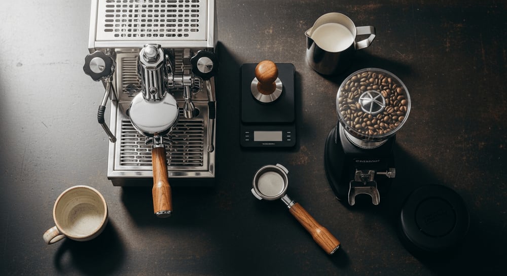 Overhead shot showcasing various barista tools arranged artistically on a dark, textured surface, emphasizing their functionality and aesthetic appeal