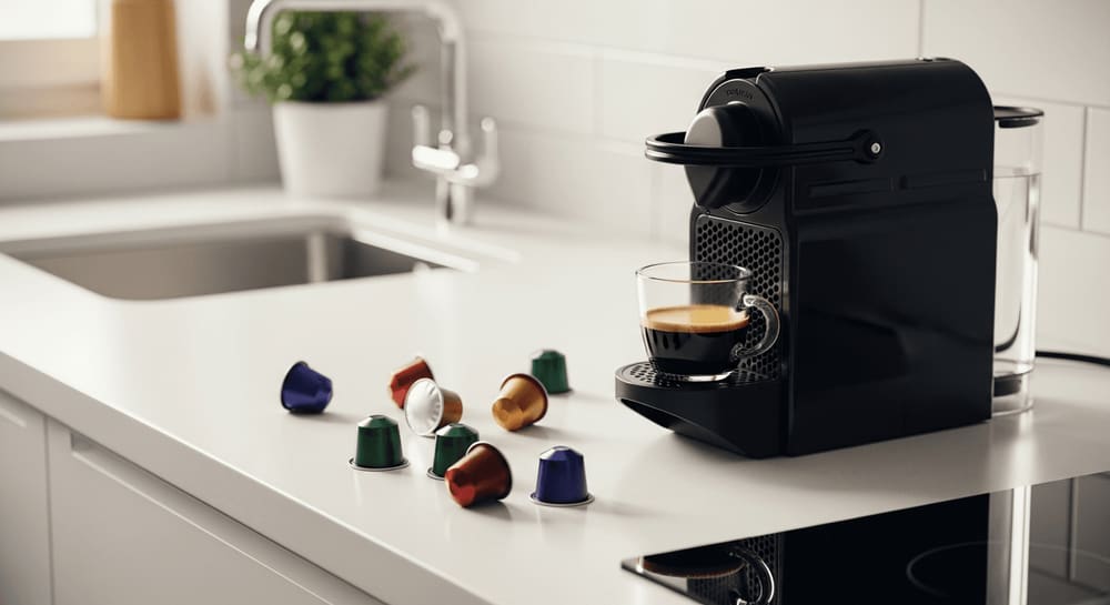 Eine elegante, moderne Küchentheke mit einer Kapselmaschine, einer Tasse frisch gebrühten Kaffees und verstreuten bunten Kapseln.