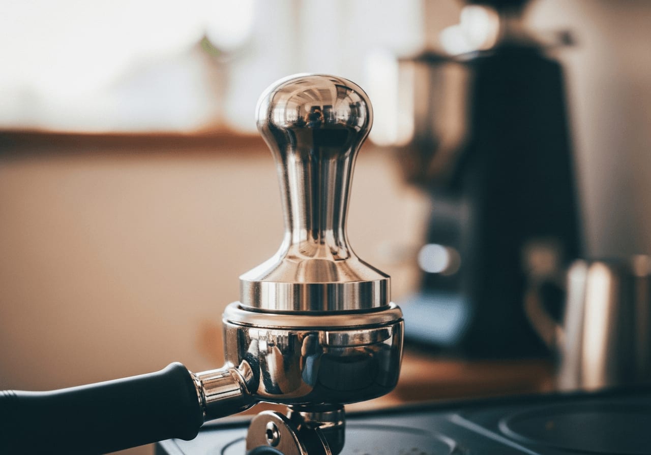 Seitenansicht eines Edelstahl-Tampers, der auf einem Bett aus frisch gemahlenem Kaffee in einem Siebträger liegt