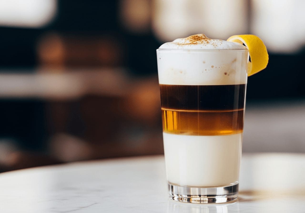 A perfectly layered Barraquito in a tall glass, showcasing distinct layers of condensed milk, liqueur, espresso, and foamed milk, garnished with lemon peel and cinnamon, soft focus background.