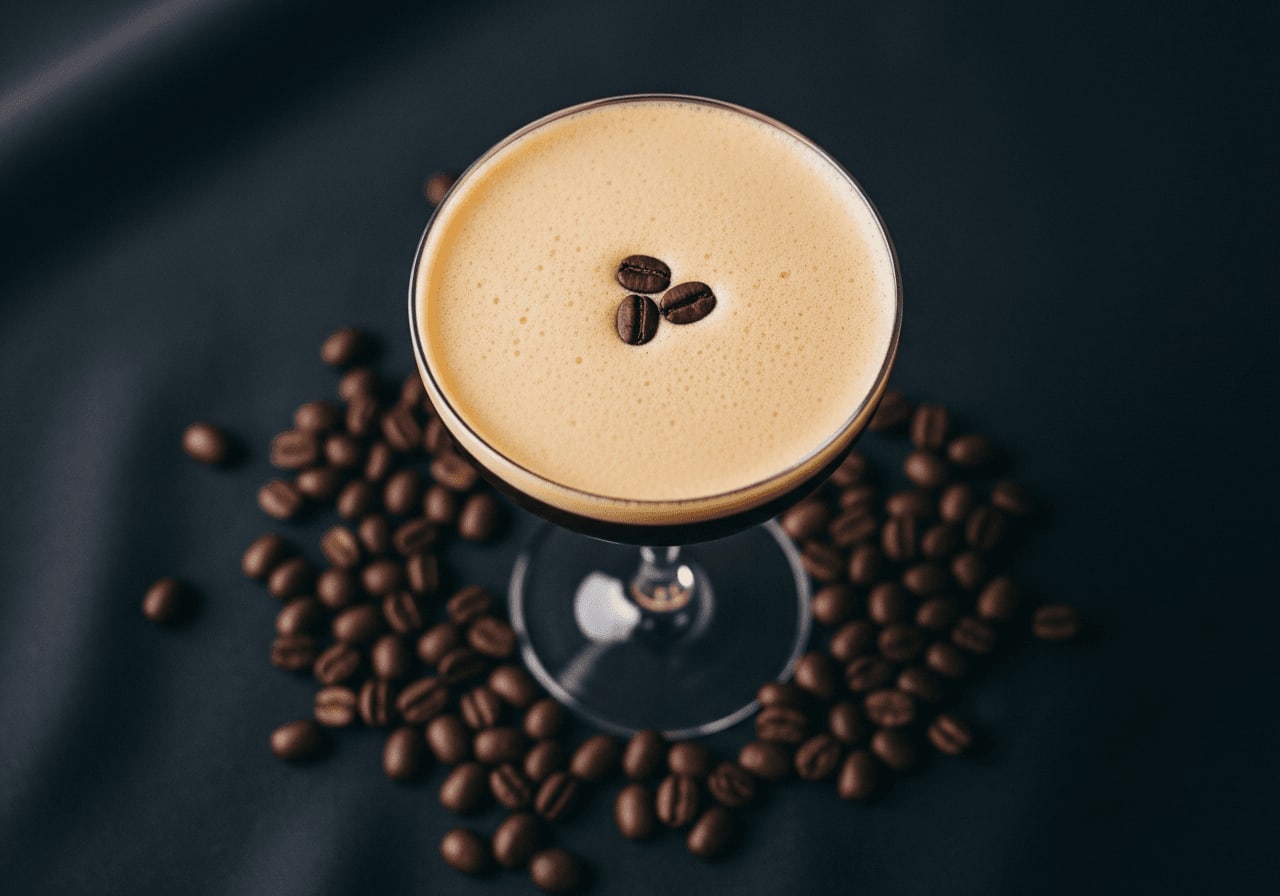 Draufsicht eines Espresso Martinis in einem Coupé-Glas, Kaffeebohnen verstreut, dunkler Hintergrund