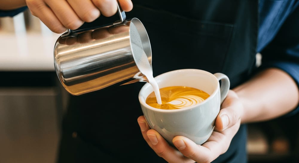 Ein Barista gießt Milchschaum in einen Espresso und demonstriert das perfekte Mischverhältnis für klassische Kaffee-Rezepte.