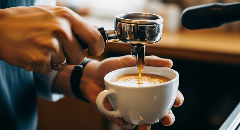 Barista-Vokabular in der Praxis: Ein Barista brüht frischen Espresso mit goldbrauner Crema in einem gemütlichen Café.
