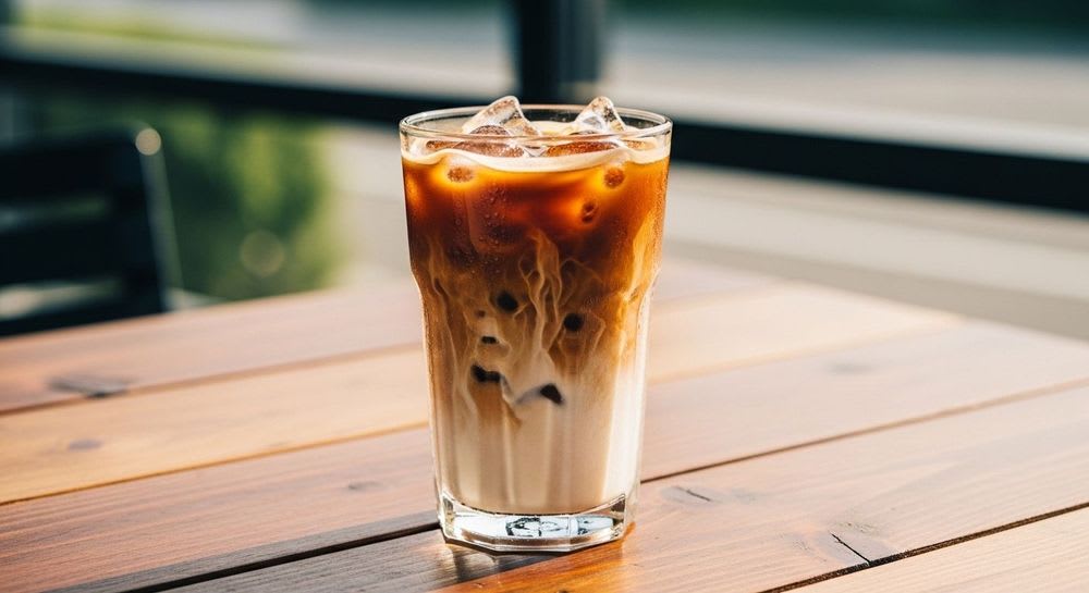 Ein großes Glas Eiskaffee ohne Zucker mit einer Milchalternative auf einem Gartentisch, eine köstliche Erfrischung ohne Reue.